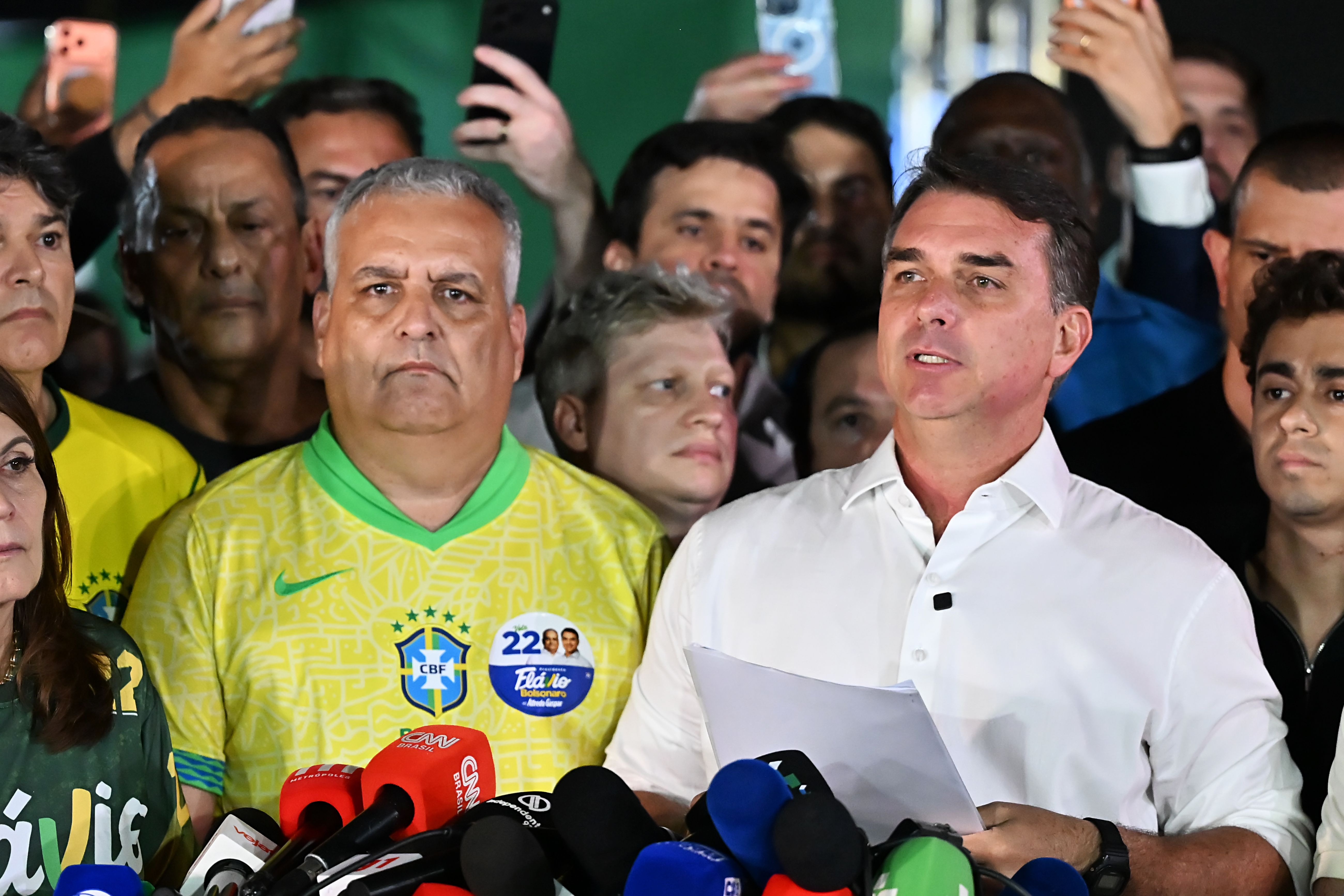 Flavio Bolsonaro spricht nach den Wahlergebnissen vor Mikrofonen und umgeben von Anhängern.