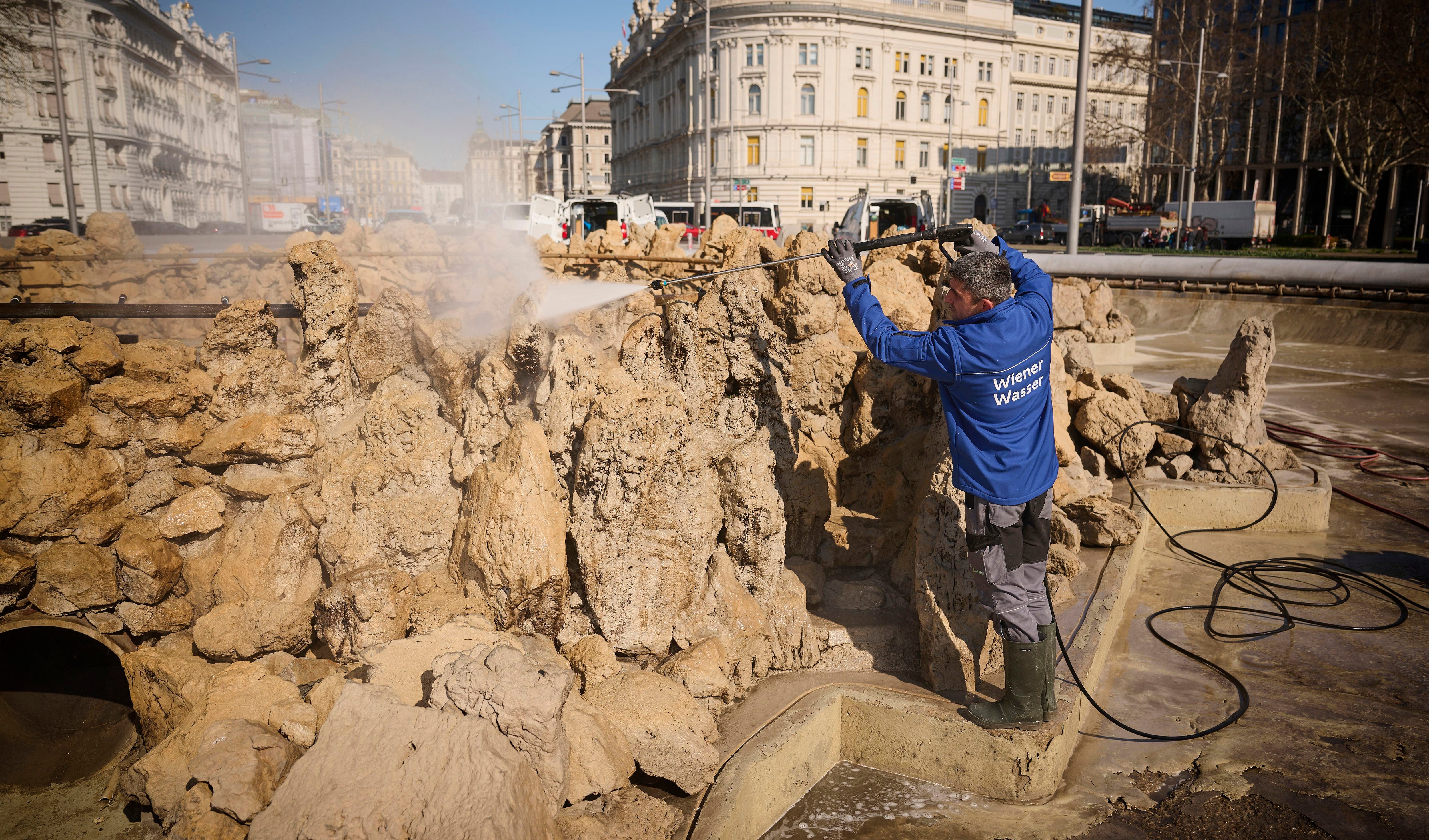 Ein Mann reinigt den Hochstrahlbrunnen in Wien mit einem Hochdruckreiniger im Frühling.