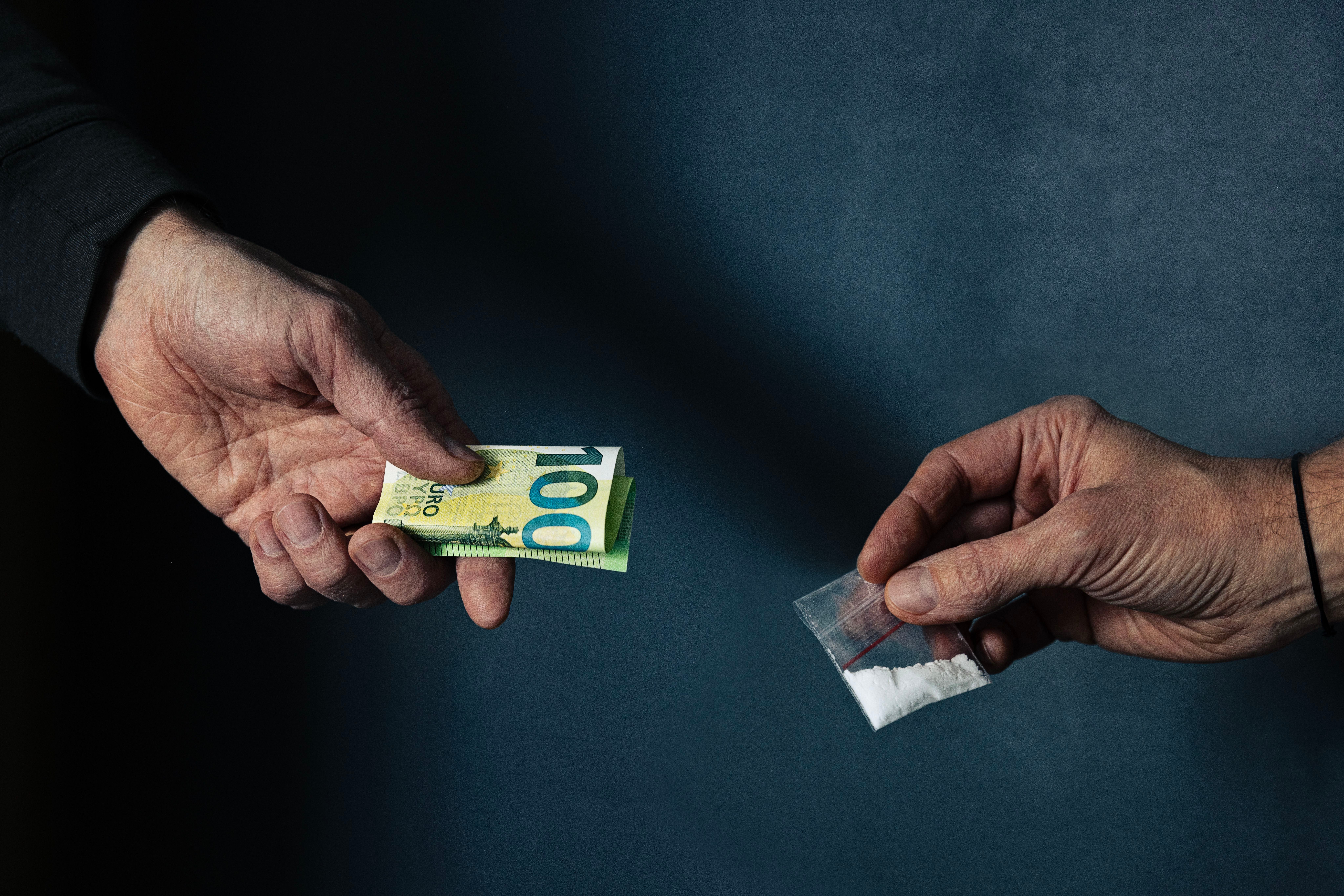Eine Hand hält 100-Euro-Schein, die andere ein Tütchen mit weißem Pulver.