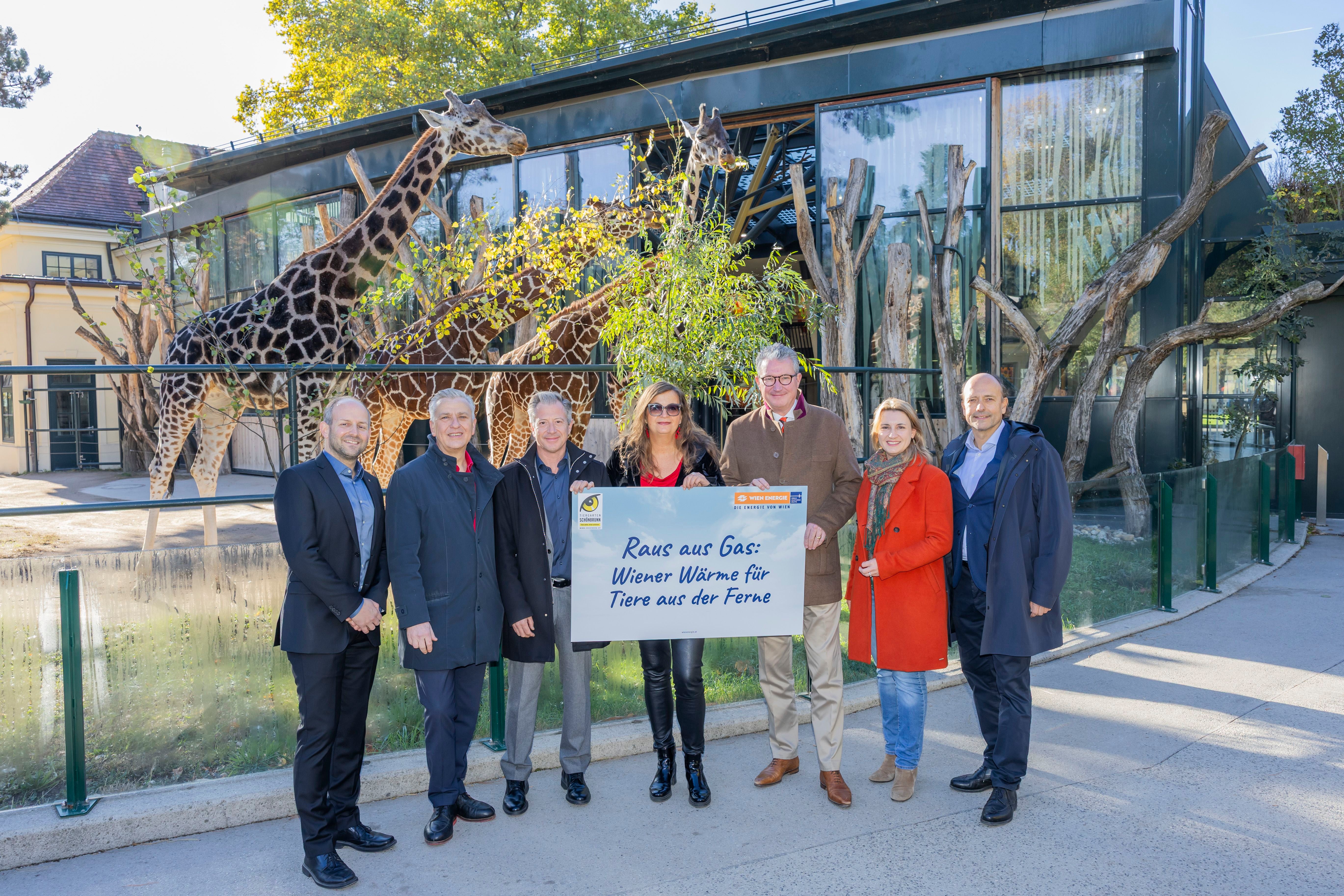 Sieben Personen stehen mit Plakat vor dem Giraffengehege im Tiergarten Schönbrunn.