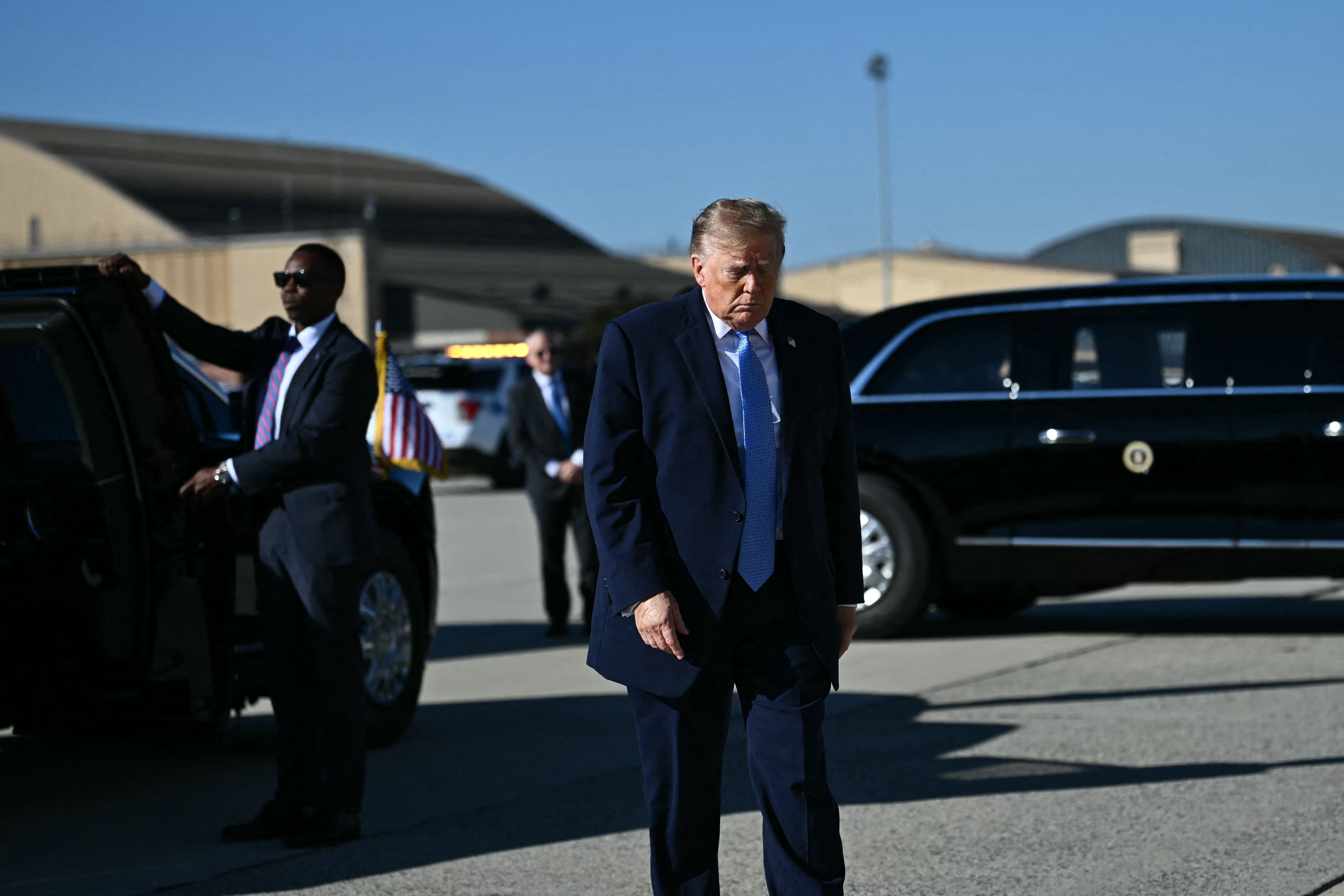 Ein Mann im Anzug läuft auf dem Rollfeld neben einer schwarzen Limousine mit US-Flagge.
