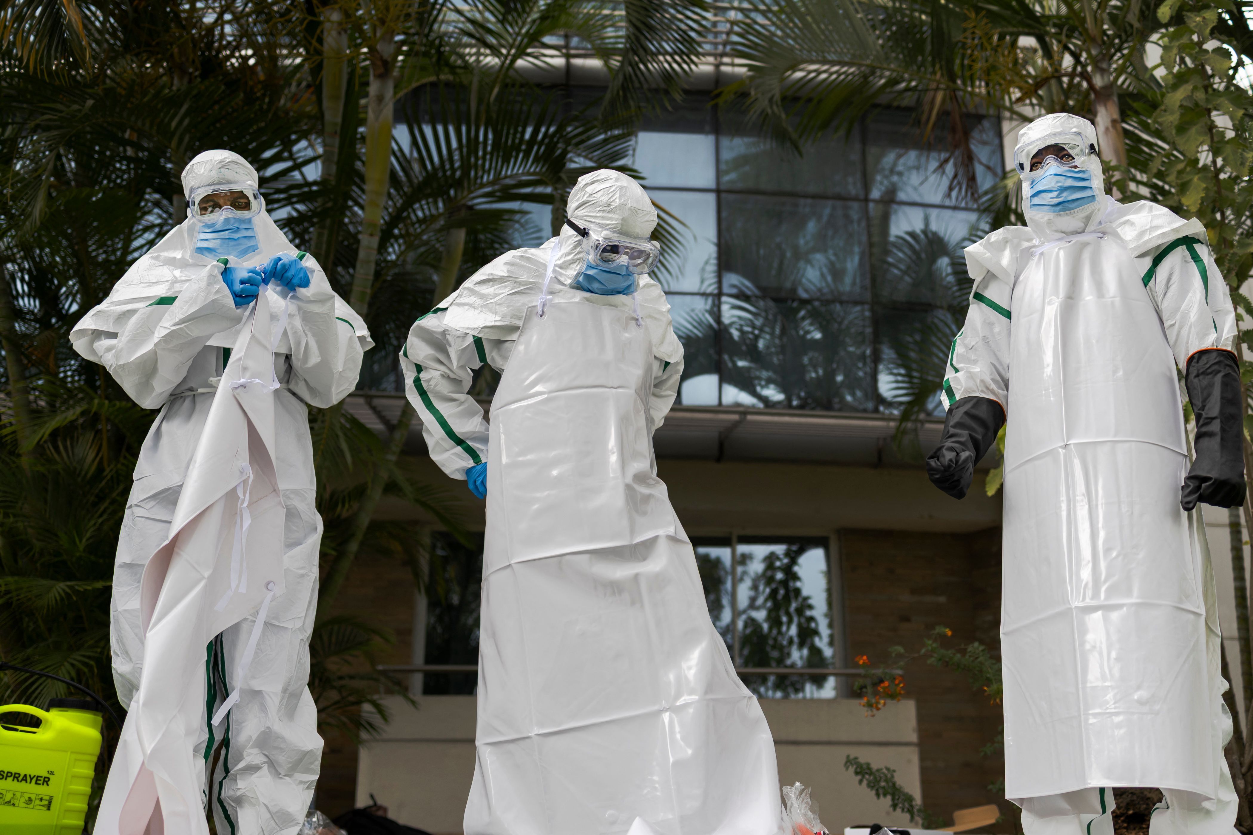 Drei Personen in Schutzkleidung simulieren den Umgang mit Ebola-Opfern im Freien vor einem Gebäude.