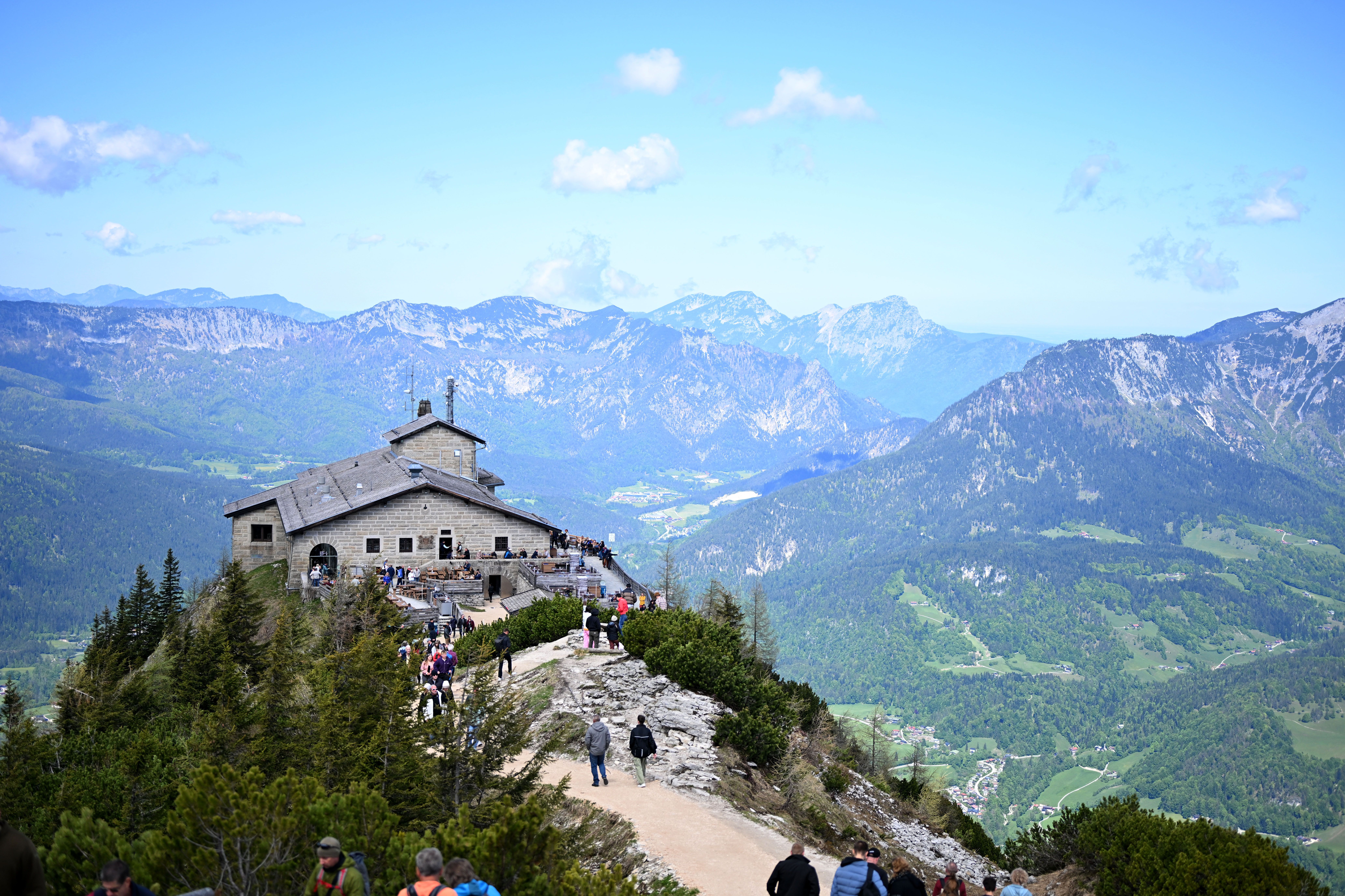 Das Kehlsteinhaus auf einem Berggipfel mit Besuchern, umgeben von Alpenlandschaft und Tälern.