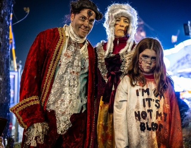 Drei Menschen in blutverschmierten Halloween-Kostümen posieren gruselig im Prater bei Nacht.