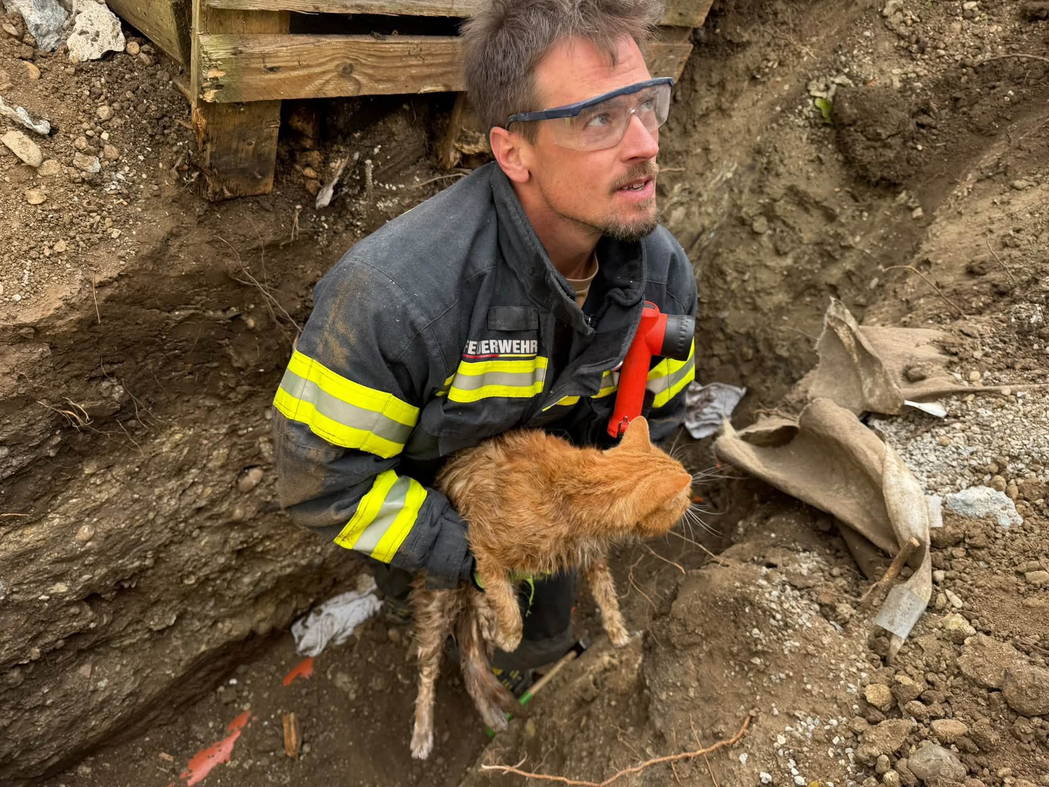 Feuerwehrmann rettet eine orangefarbene Katze aus einer Grube.