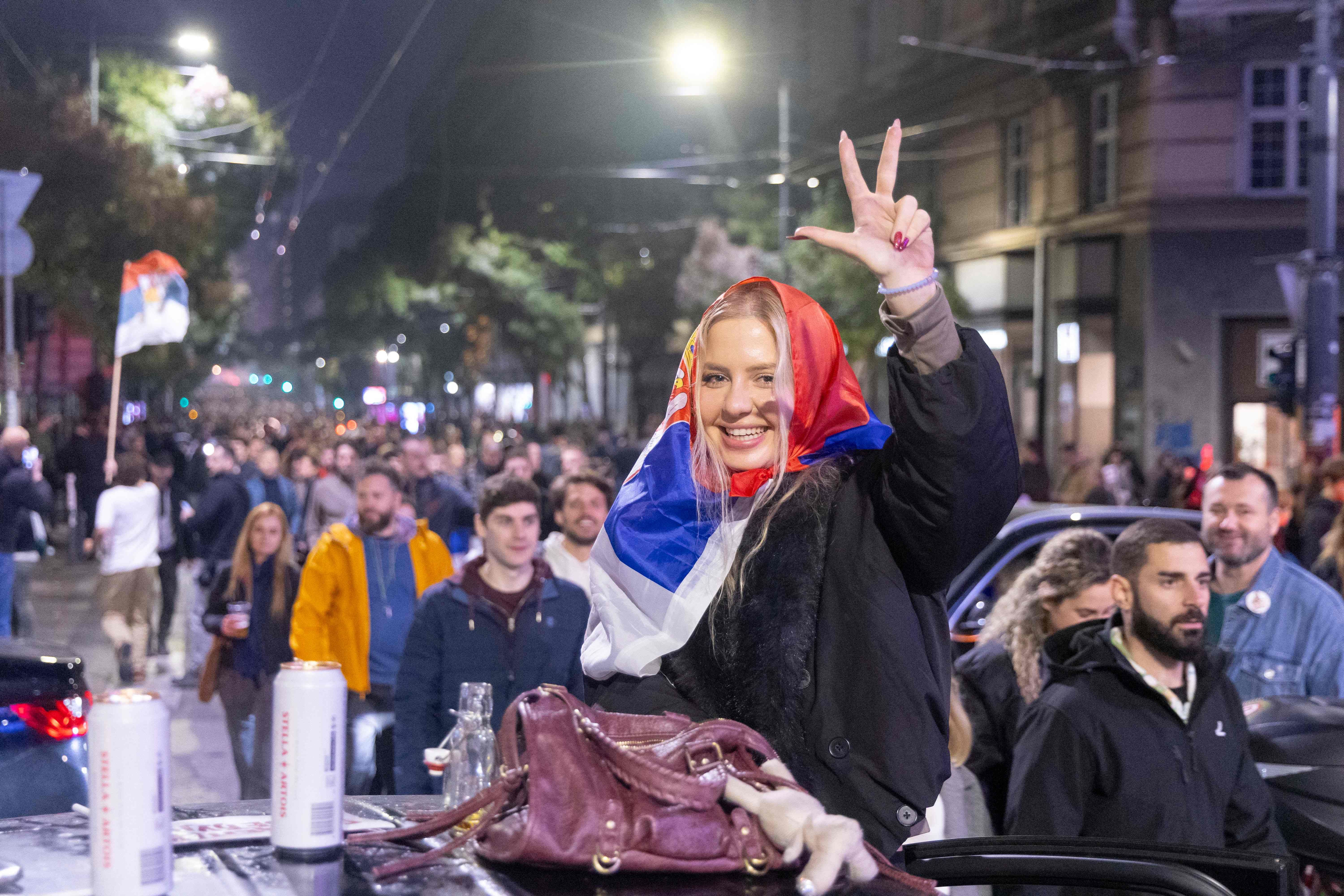 Junge Frau feiert mit serbischer Flagge auf offener Straße bei einer Wahl-Siegesfeier in Belgrad.