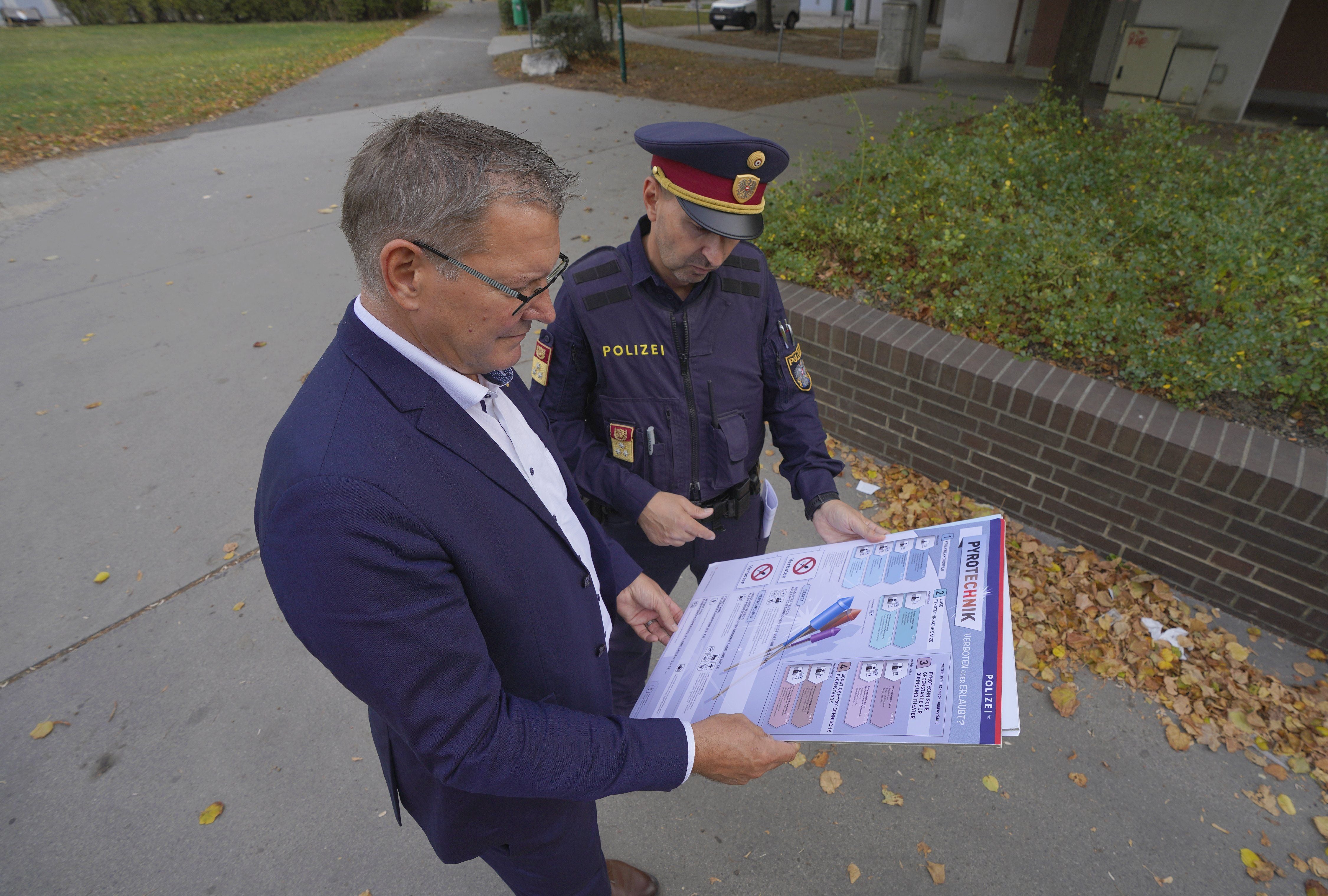 Ein Polizist und ein Mann im Anzug betrachten draußen gemeinsam ein großes Informationsplakat.