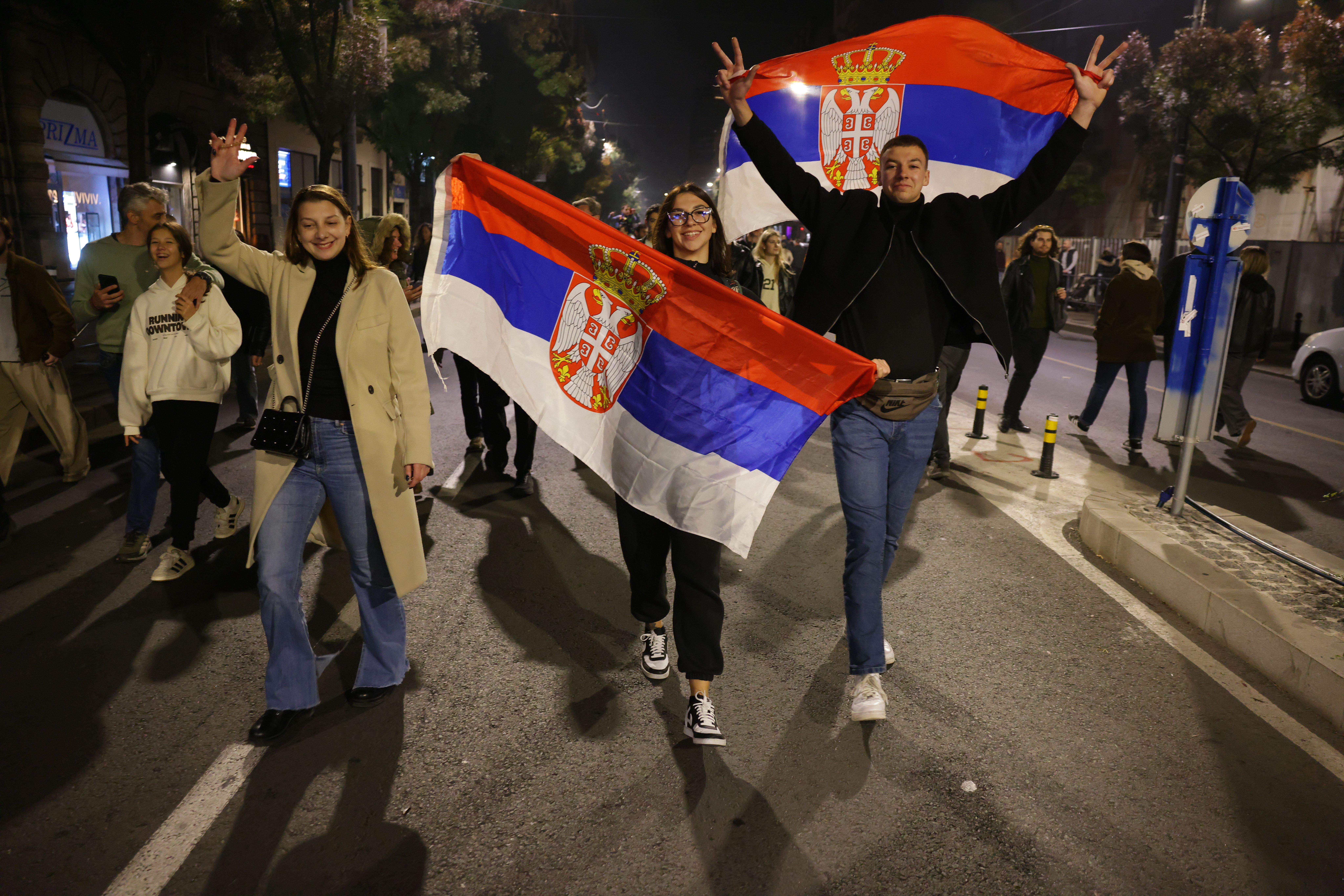 Menschen feiern mit serbischen Flaggen nach den Parlamentswahlen in Belgrad bei Nacht.