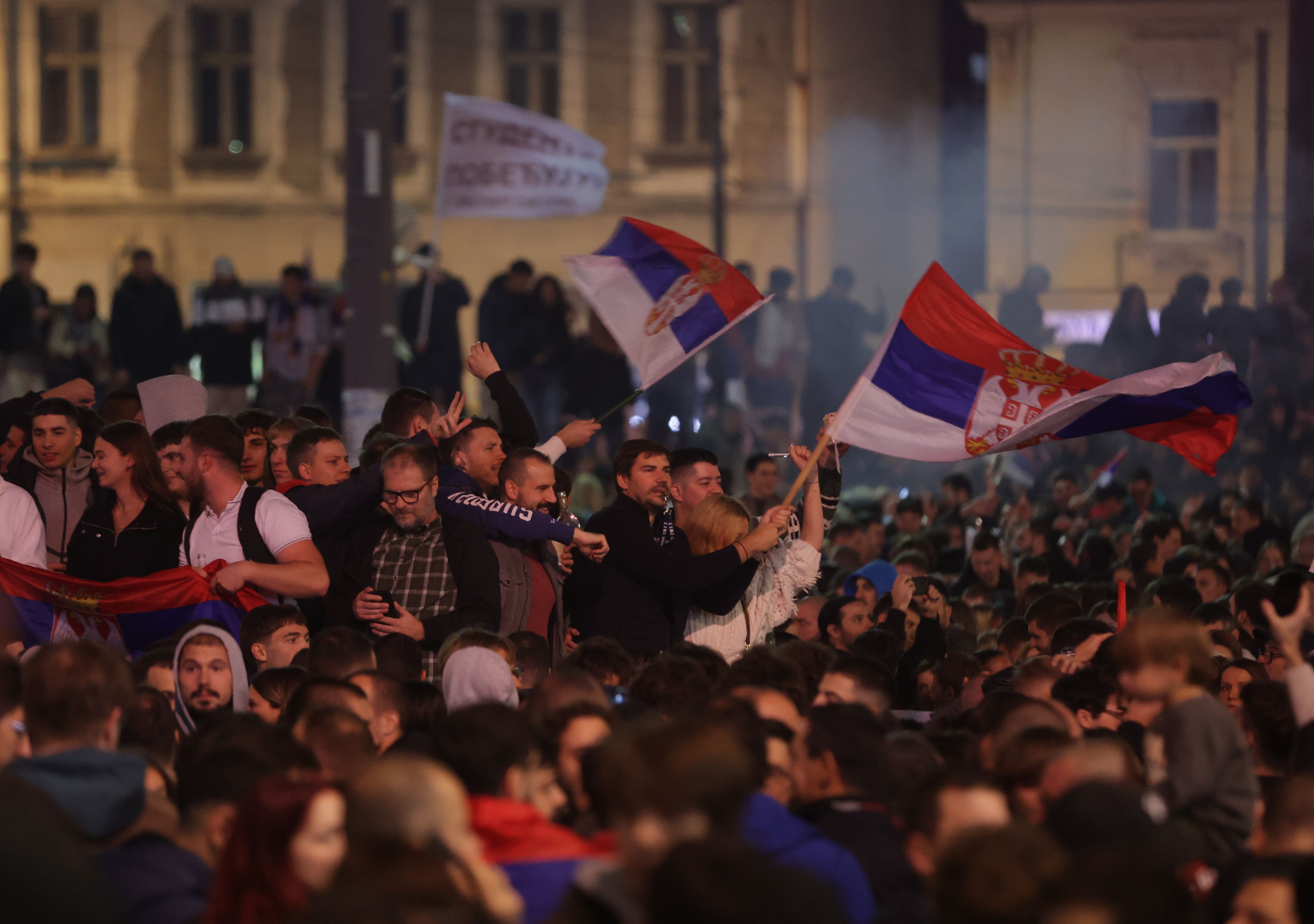 Menschenmenge mit serbischen Fahnen feiert nachts nach den Parlamentswahlen in Belgrad.