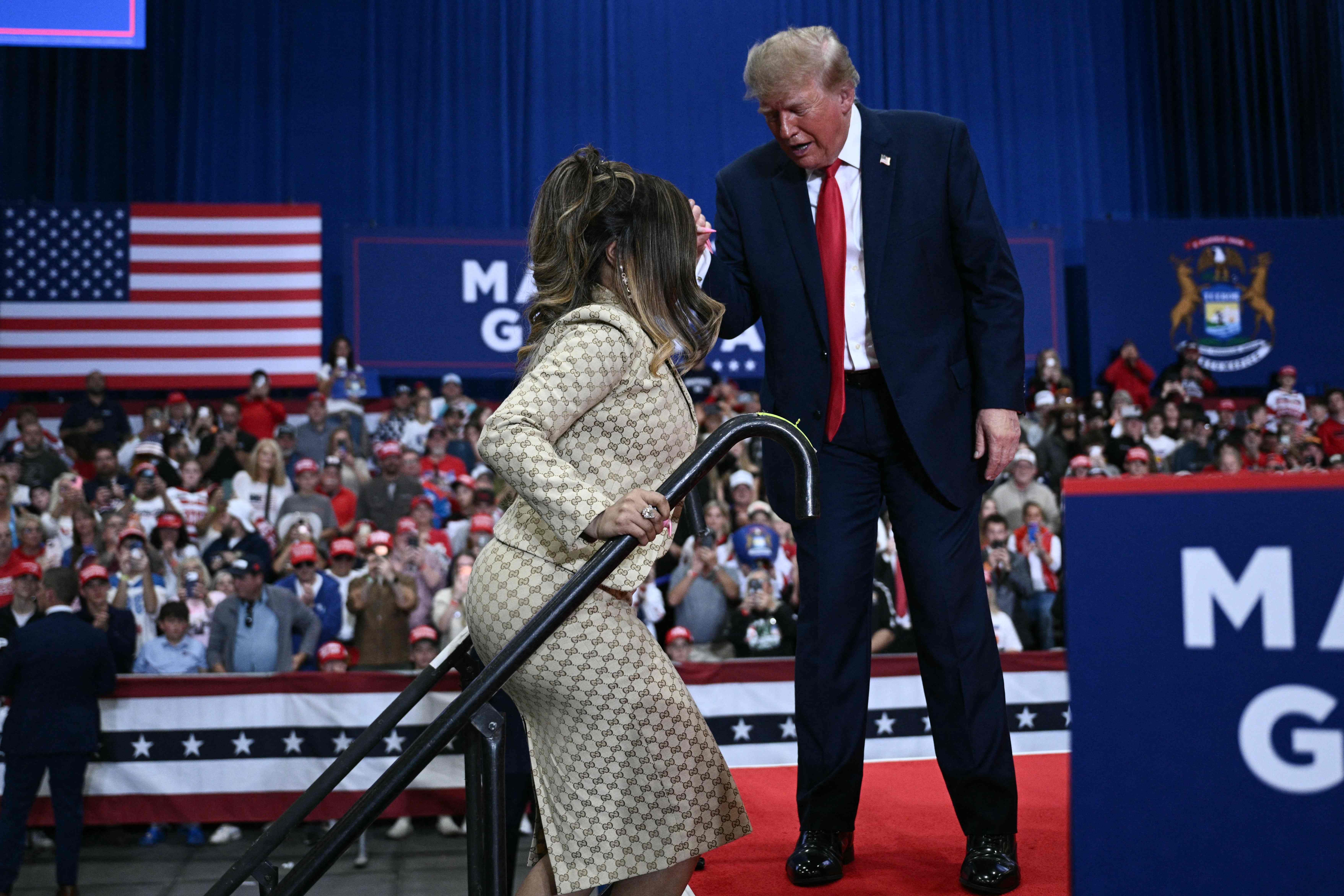 Donald Trump hilft einer Frau beim Betreten der Bühne vor einer jubelnden Menschenmenge.
