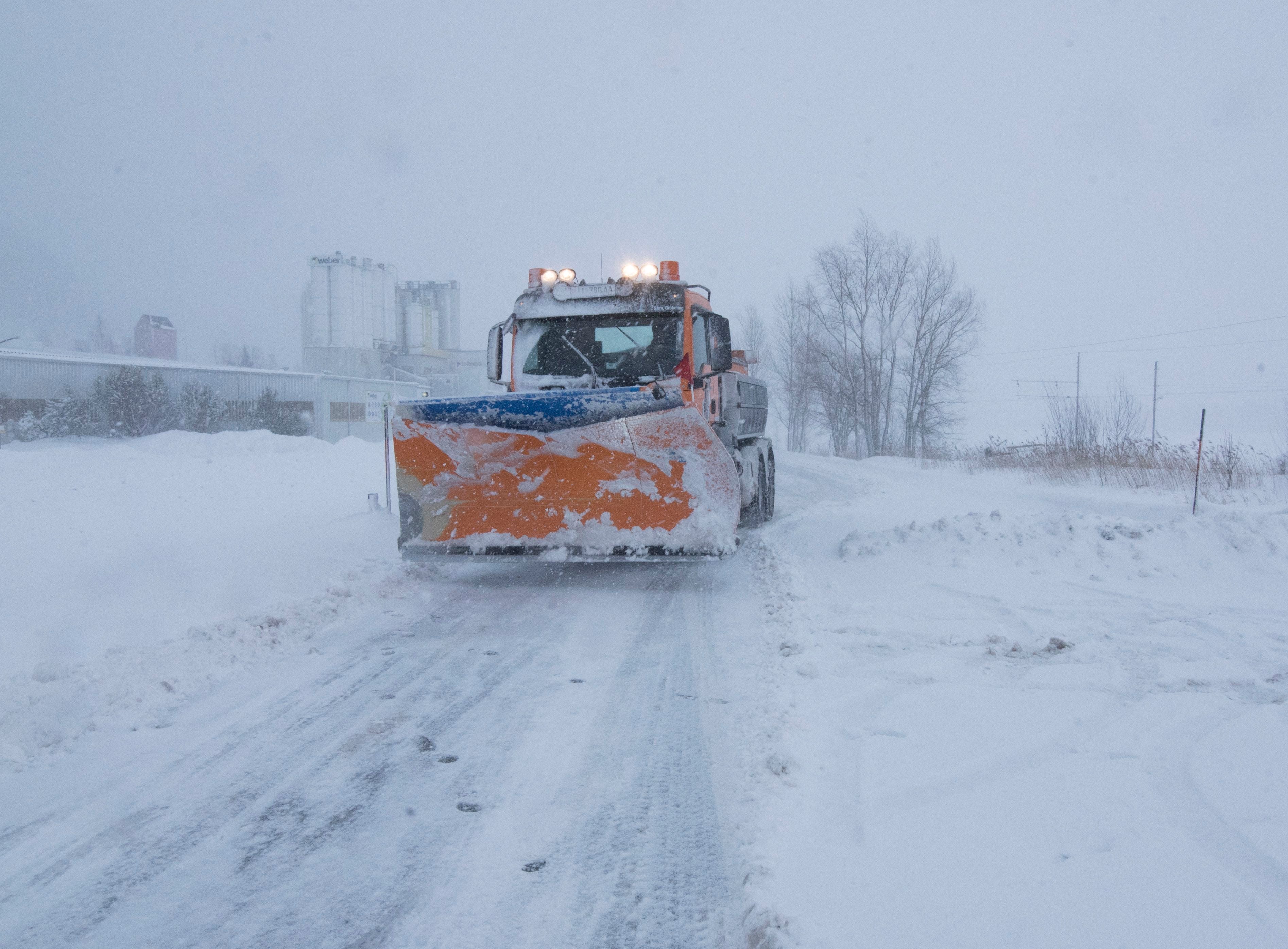Ein Schneepflug räumt eine verschneite Landstraße bei winterlichem Schneefall.