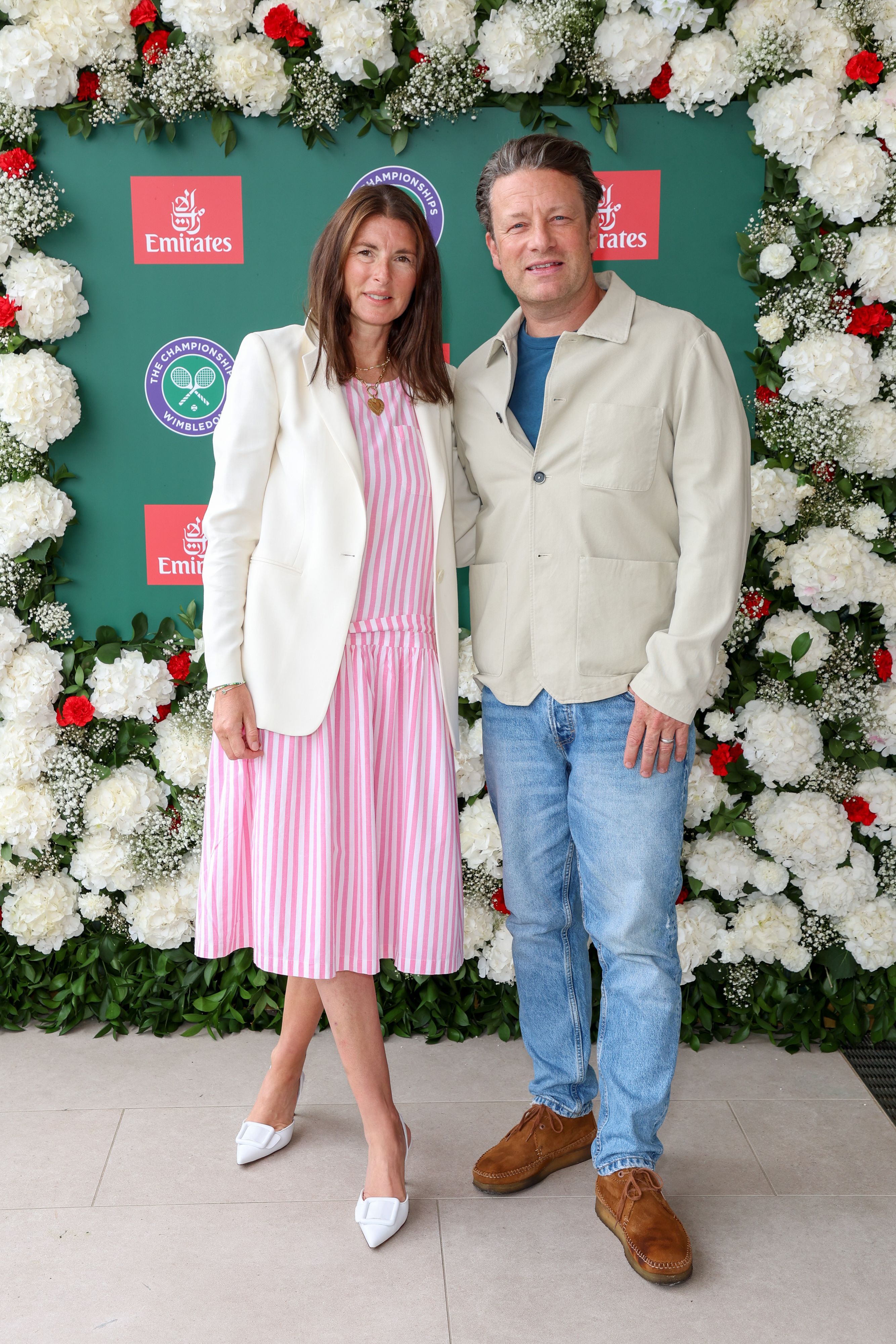 Ein Mann und eine Frau posieren vor einer Wand mit weißen und roten Blumen und Wimbledon-Logos.