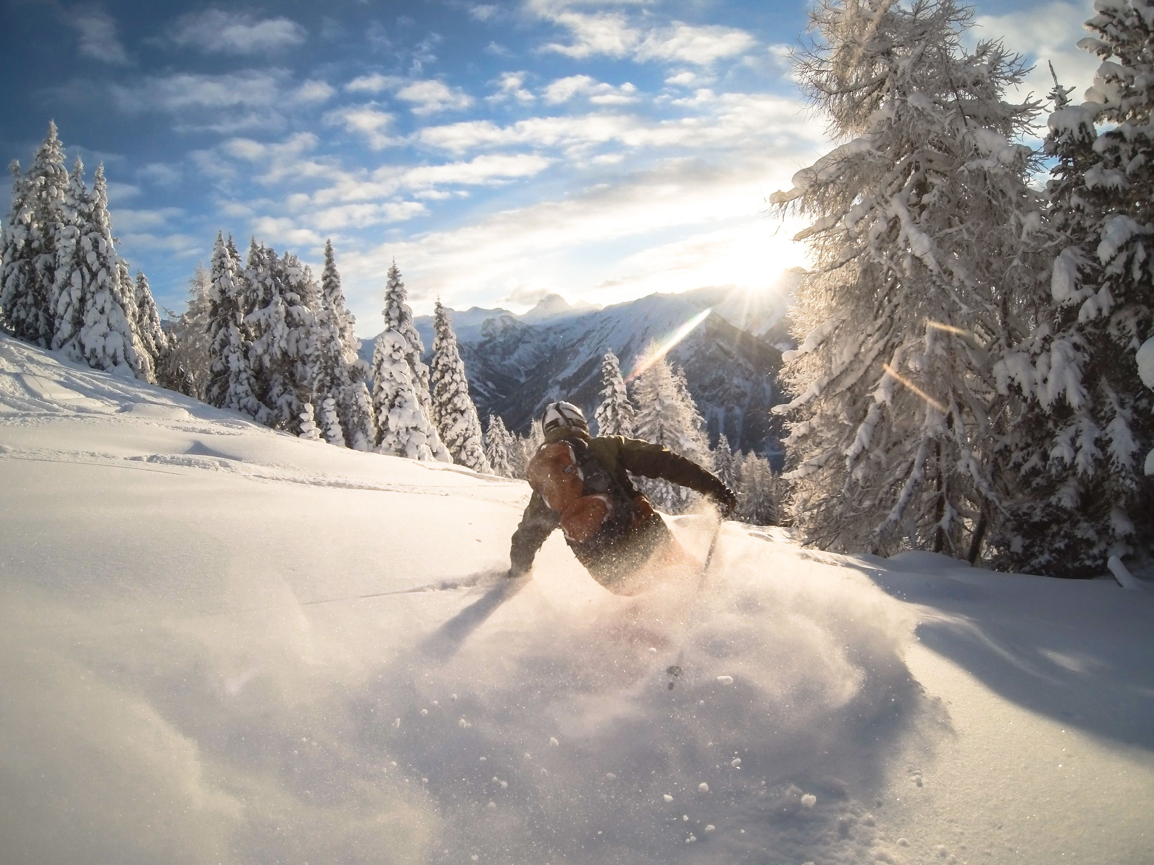 Skifahrer fährt durch frischen Pulverschnee im verschneiten Gebirgswald bei Sonnenschein.