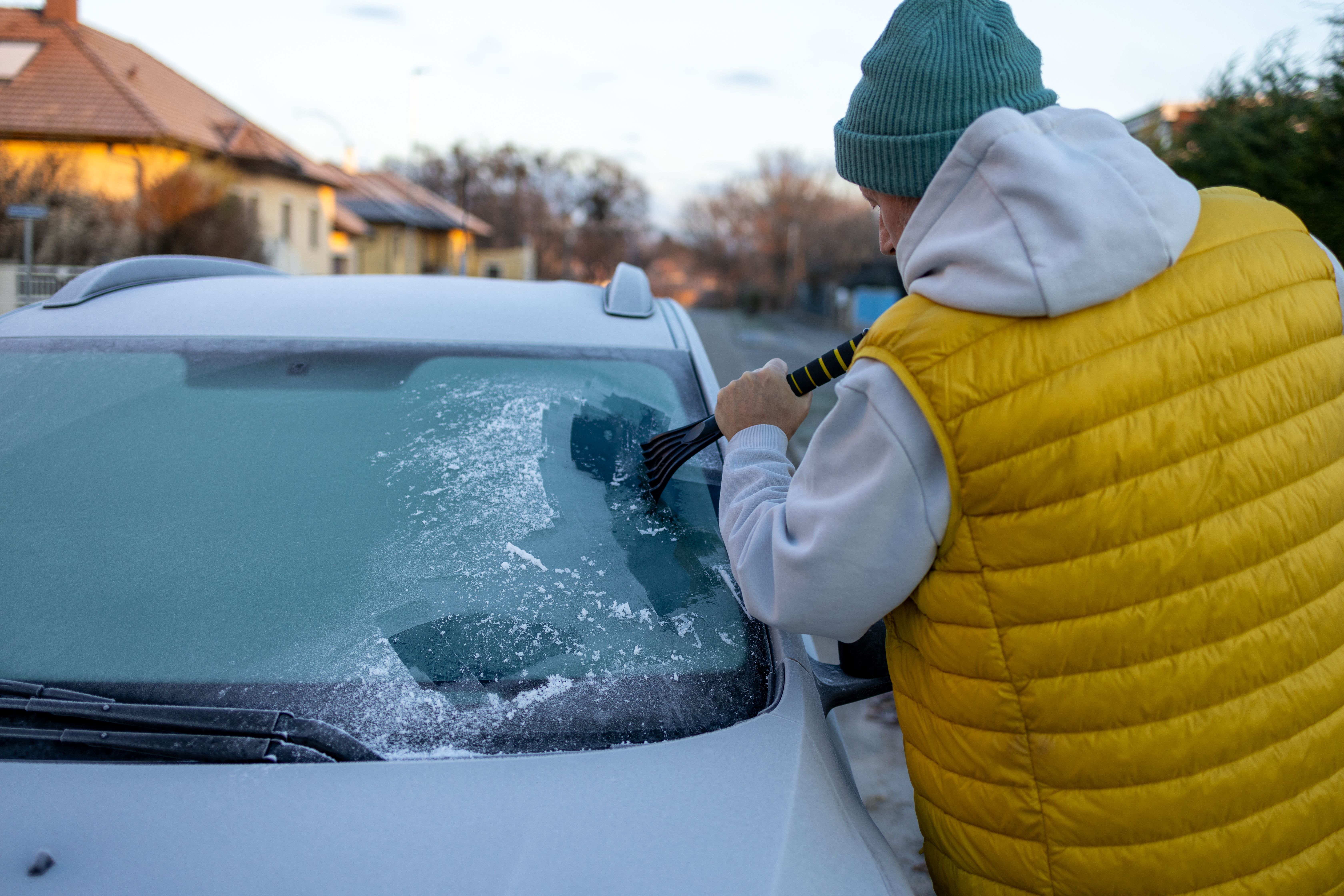 Älterer Mann kratzt mit Eiskratzer Schnee von der vereisten Windschutzscheibe eines Autos.