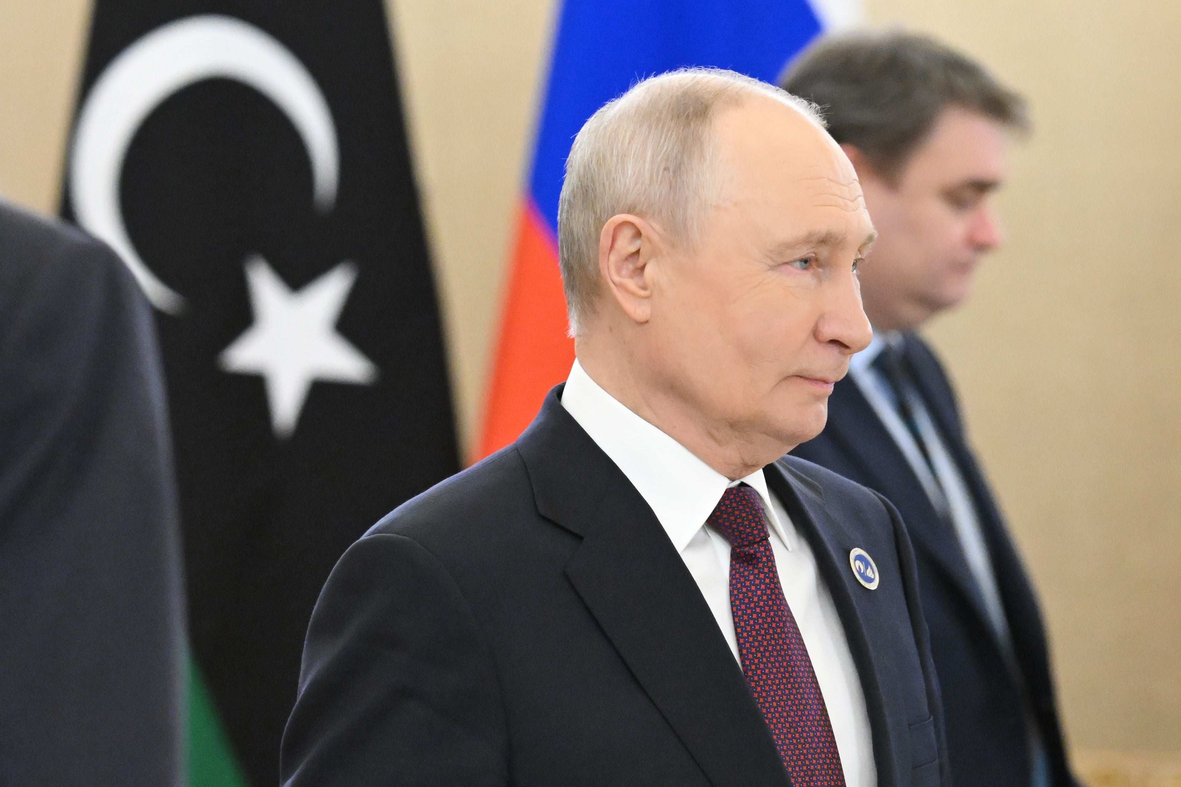Ein Mann im Anzug steht vor den Flaggen Libyens und Russlands bei einem Gipfeltreffen.