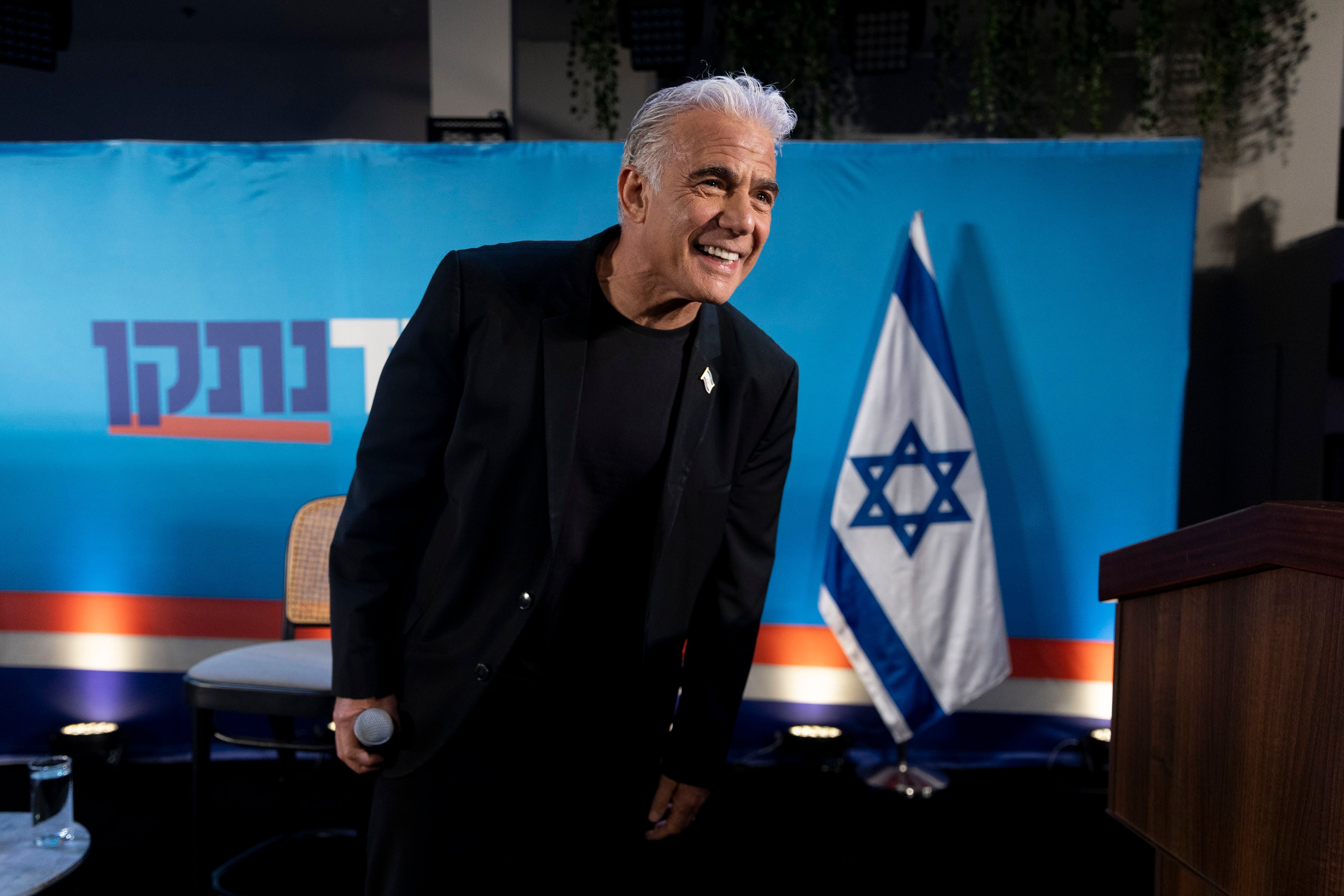 Ein Mann spricht bei einer Wahlkampfveranstaltung vor einer israelischen Flagge und einem blauen Hintergrund.
