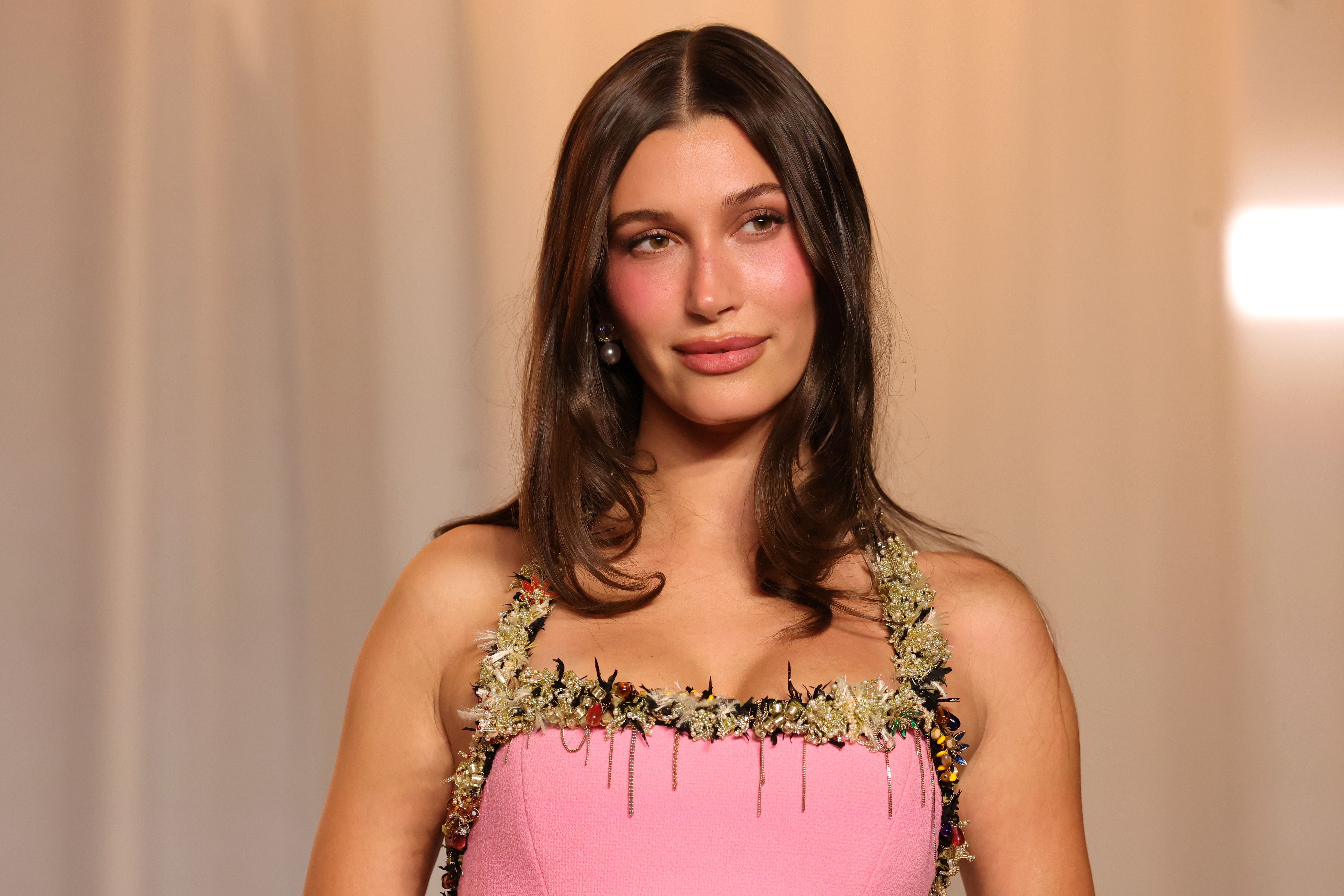 Frau mit langen braunen Haaren trägt ein pinkes Kleid mit Blumenverzierungen an den Trägern.