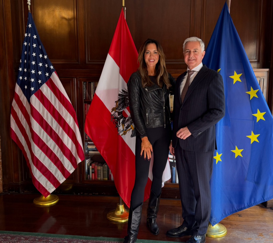 Martina Reuter und ein Mann stehen vor den Flaggen der USA, Österreichs und der EU.