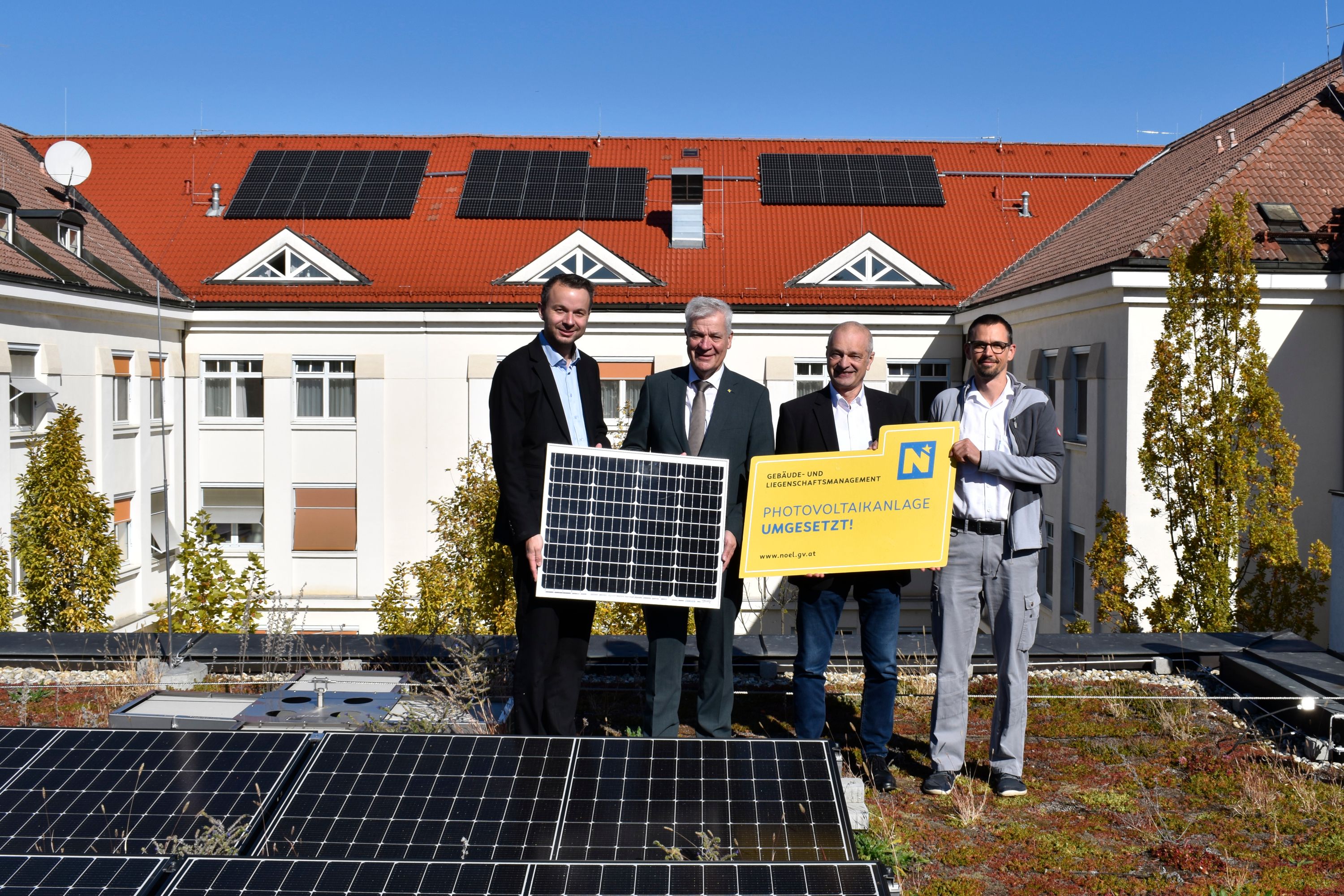 Vier Männer stehen vor Solarpaneelen am Landesklinikum Hollabrunn mit einem Schild zur PV-Anlage.