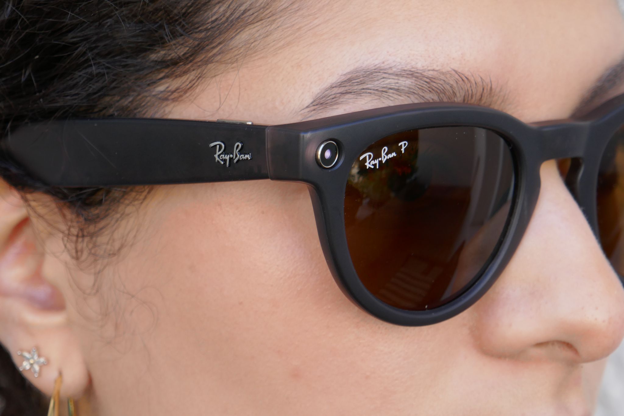 Eine Frau trägt eine schwarze Ray-Ban-Meta-Datenbrille mit kleiner LED-Anzeige am Brillengestell.