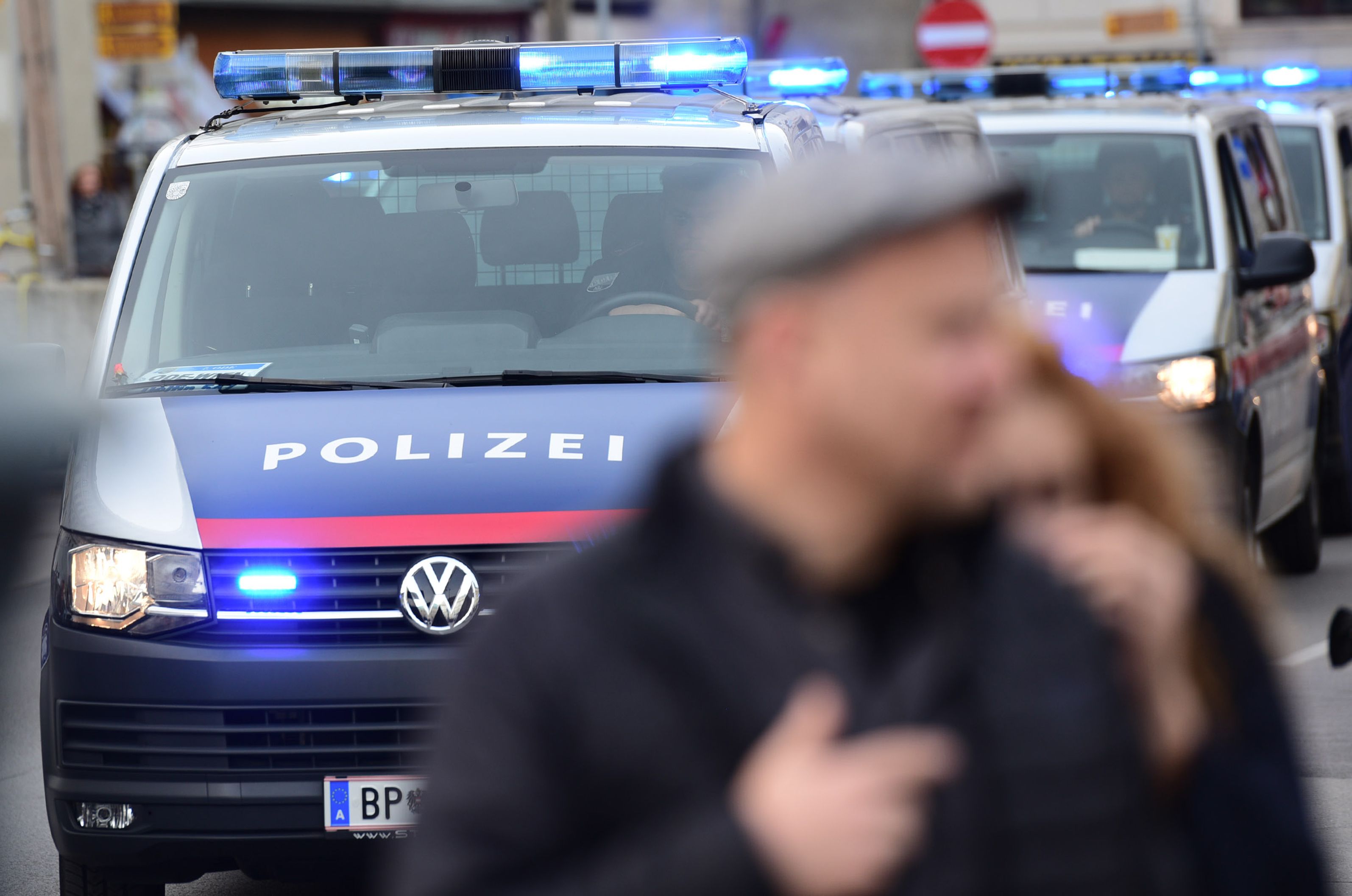 Mehrere Polizeiwagen mit Blaulicht in Wien, unscharfe Passanten im Vordergrund.