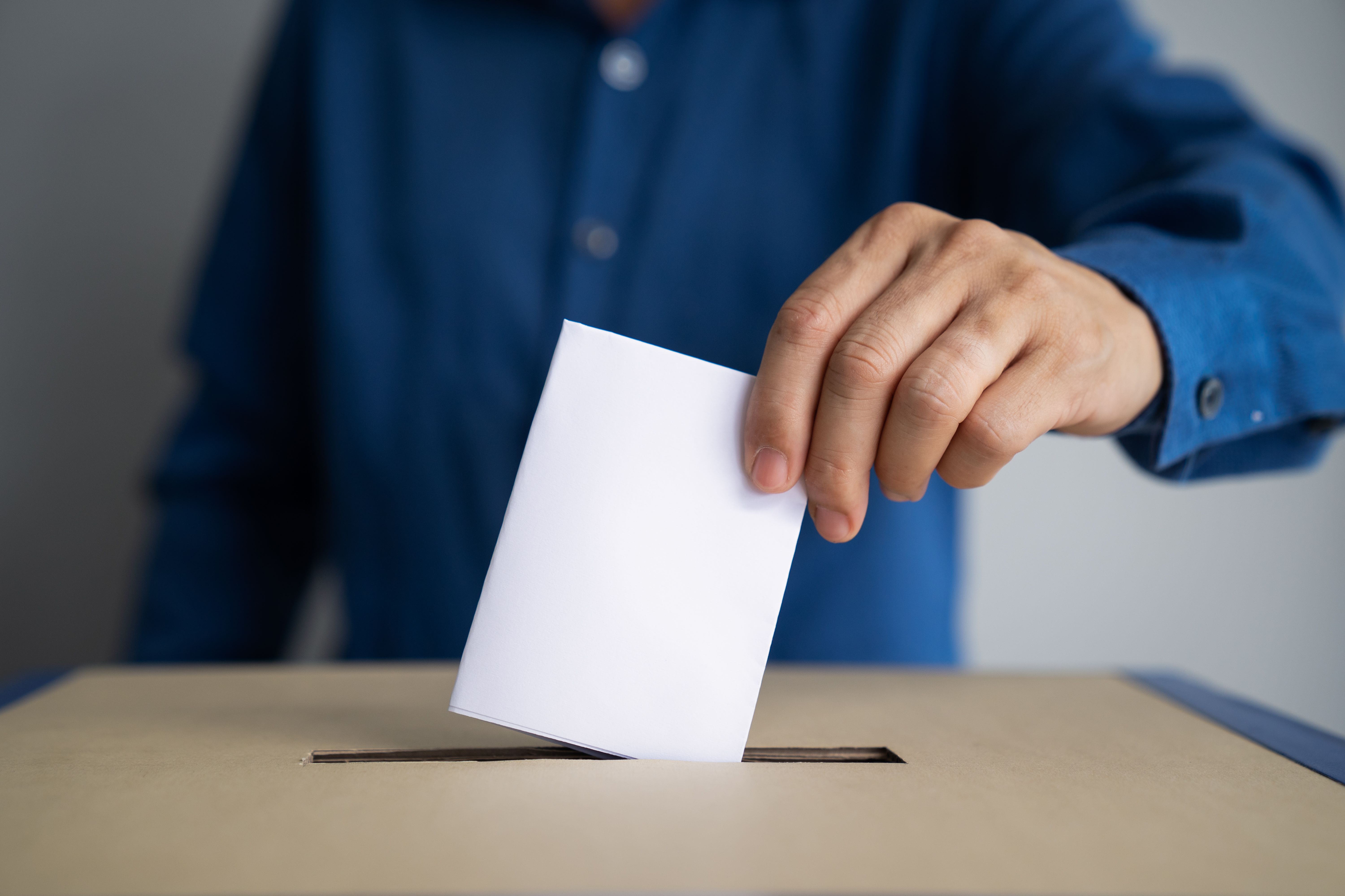 Person wirft einen Stimmzettel in eine Wahlurne.