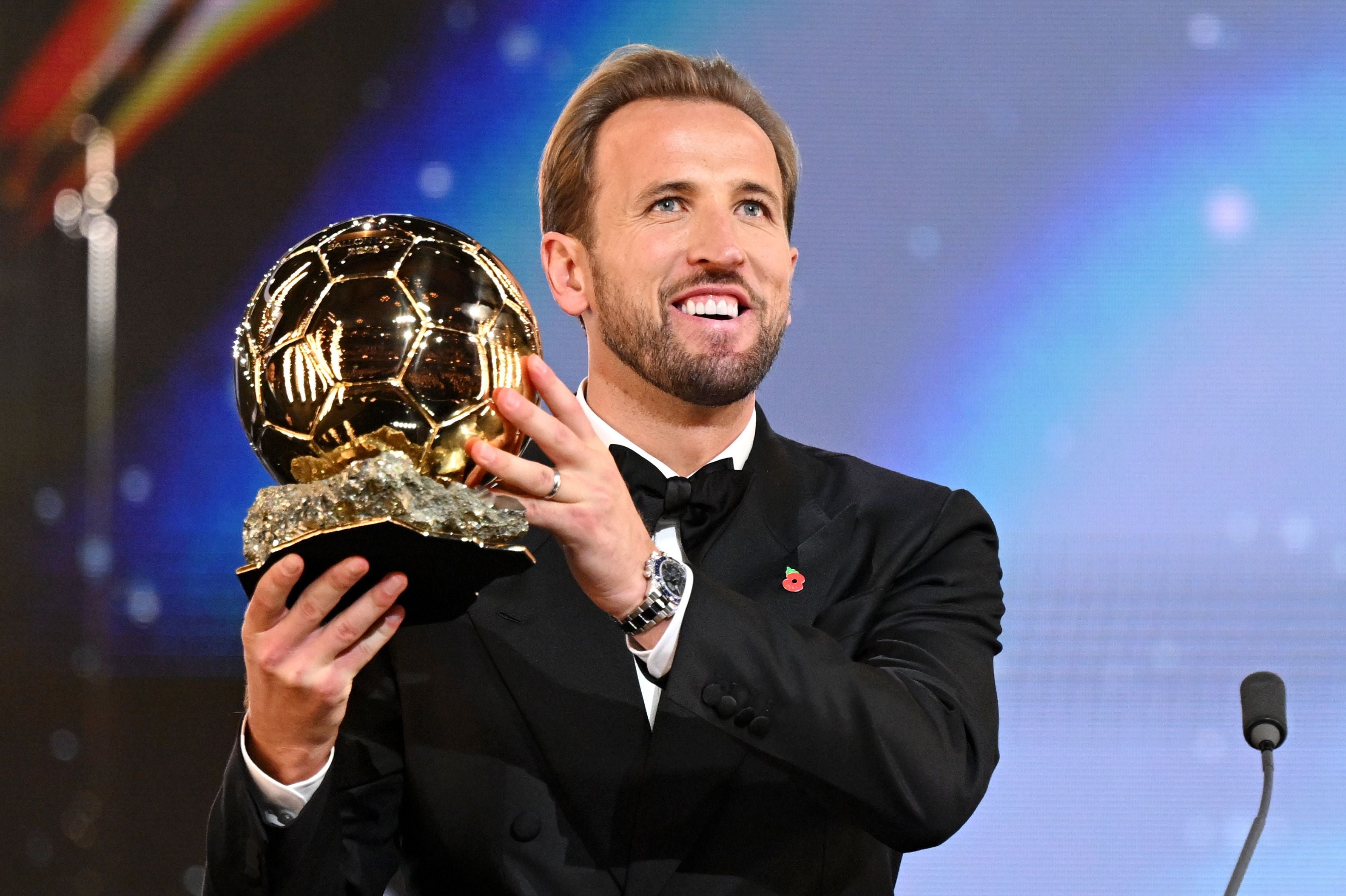 Ein Mann im Anzug hält lächelnd einen goldenen Ballon d'Or-Pokal in die Höhe.