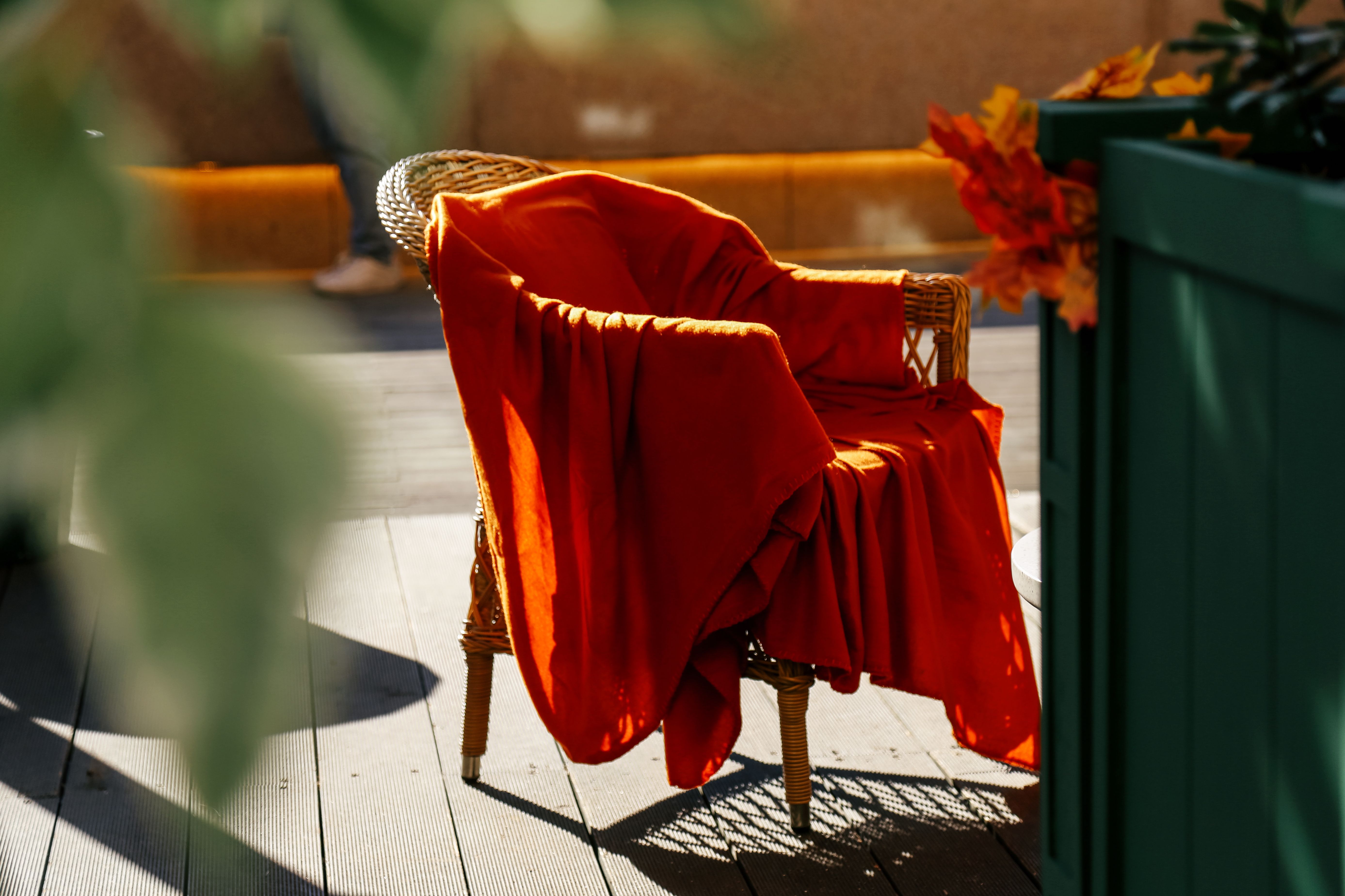 Geflochtener Stuhl mit orangefarbener Decke auf sonniger Terrasse im Herbst.