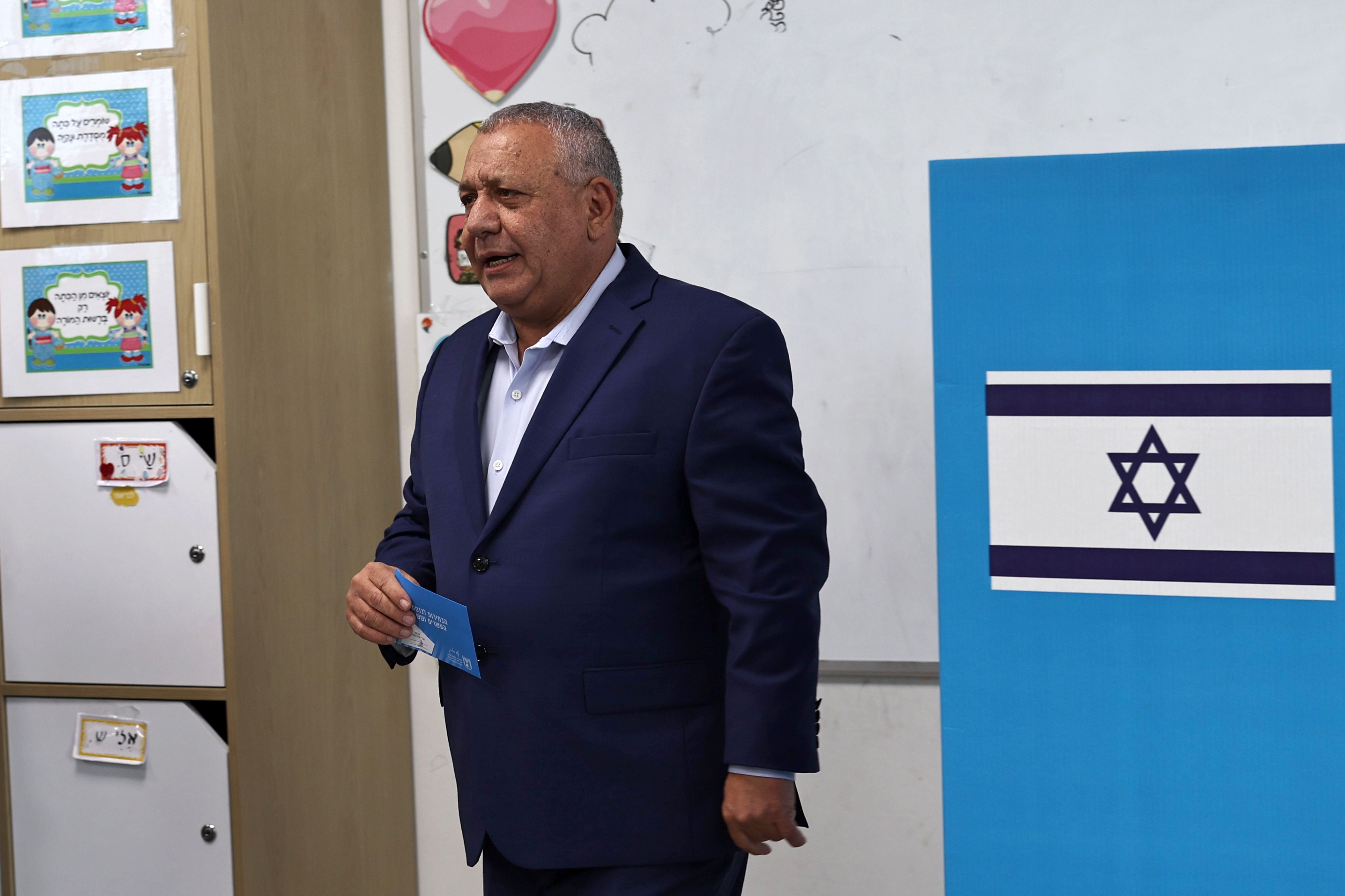 Ein Mann in Anzug steht vor einer Wahlurne mit israelischer Flagge in einem Wahllokal.