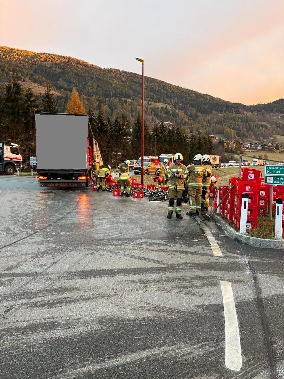 Feuerwehrleute räumen zahlreiche Bierkisten und zerbrochene Flaschen auf einer Straße auf.