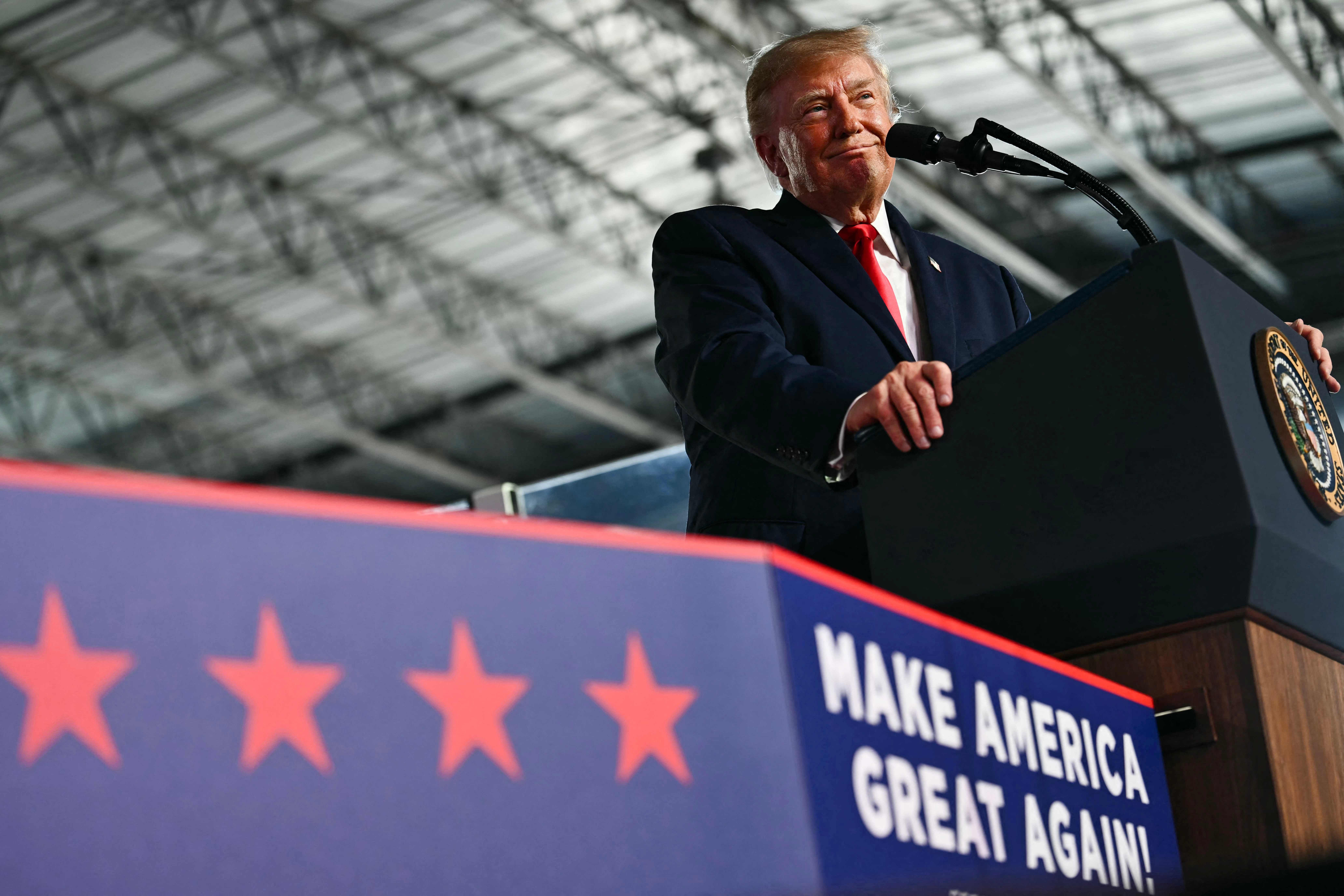 Ein Mann im Anzug spricht bei einer Wahlkampfveranstaltung am Rednerpult mit "Make America Great Again!"