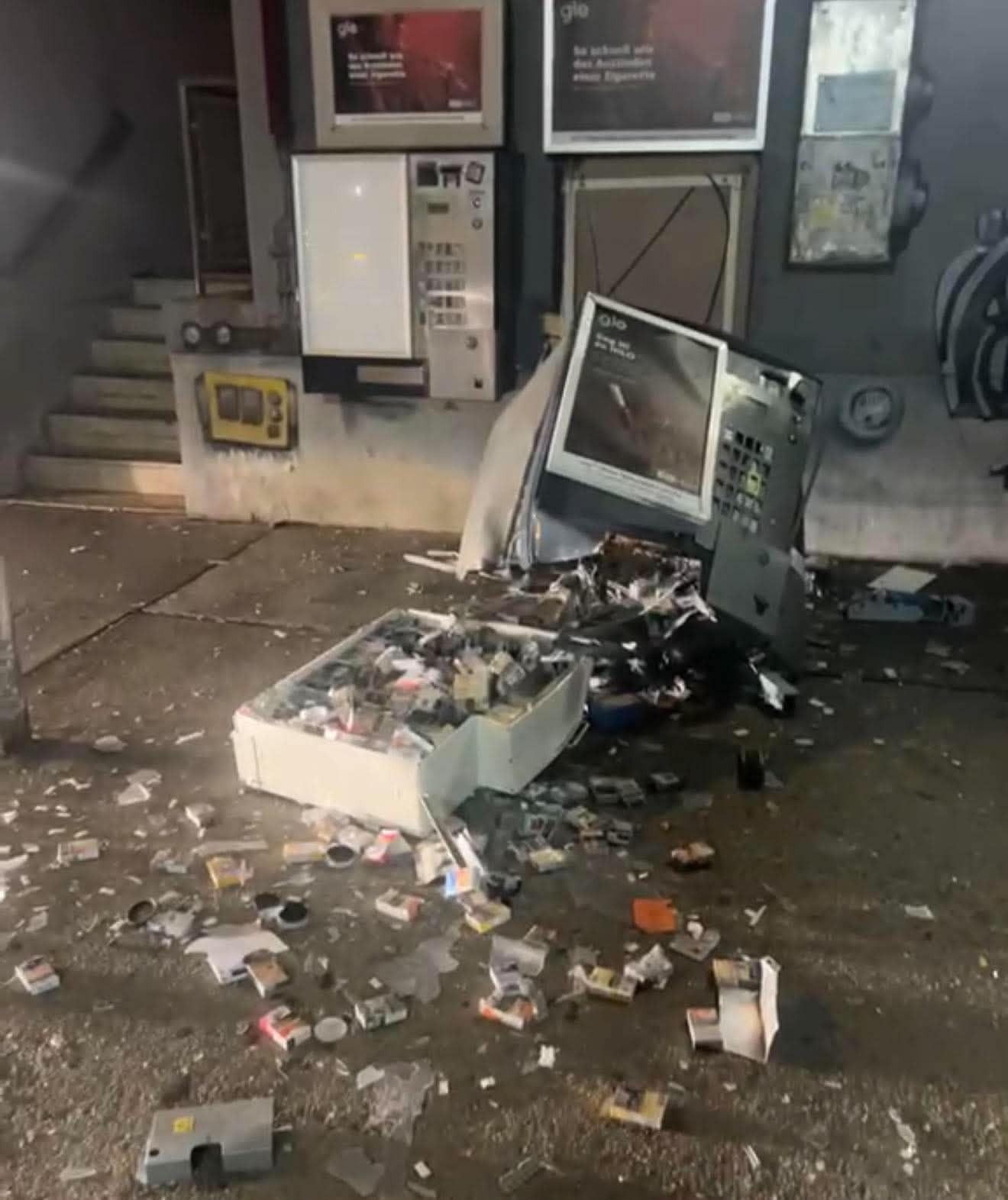 Ein zerstörter Zigarettenautomat mit verstreuten Zigarettenschachteln und Trümmern auf dem Boden.