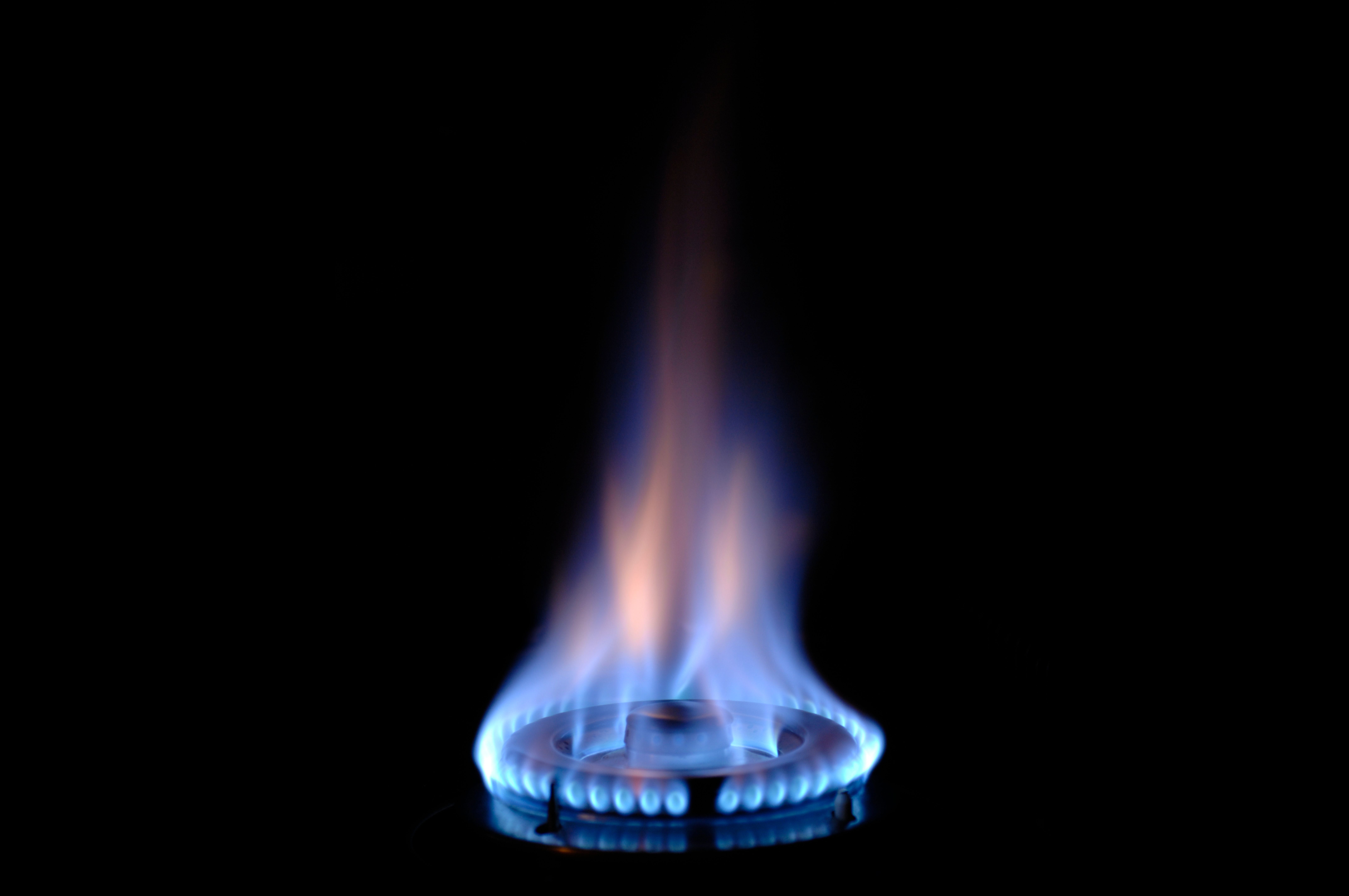 Eine blaue Gasflamme brennt auf einem Herd im Dunkeln.