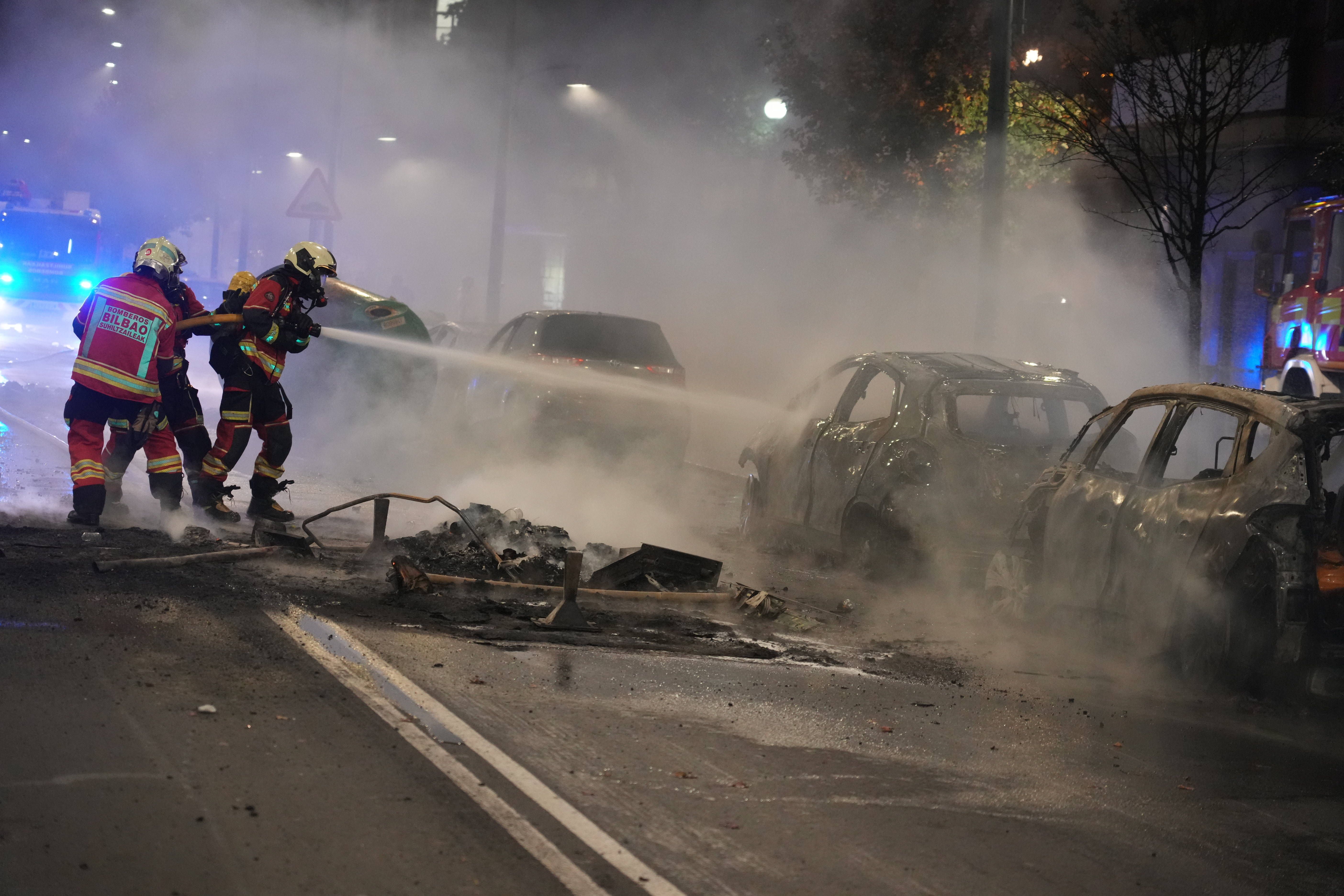 Feuerwehrleute löschen brennende Autos auf einer verrauchten Straße bei Nacht in Bilbao.