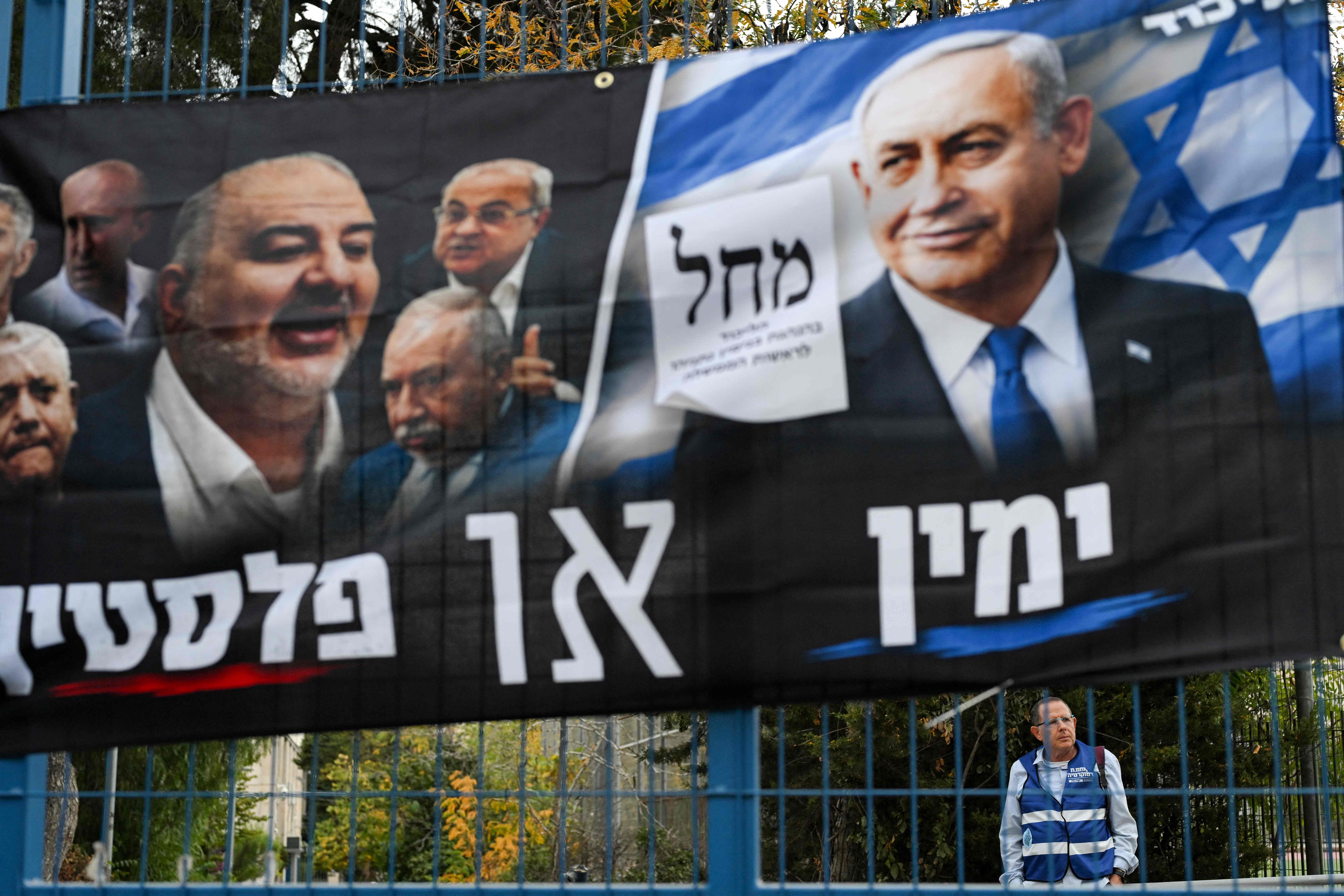 Ein Wahlbanner für Netanjahus Likud-Partei hängt an einem Zaun, ein Helfer steht dahinter.