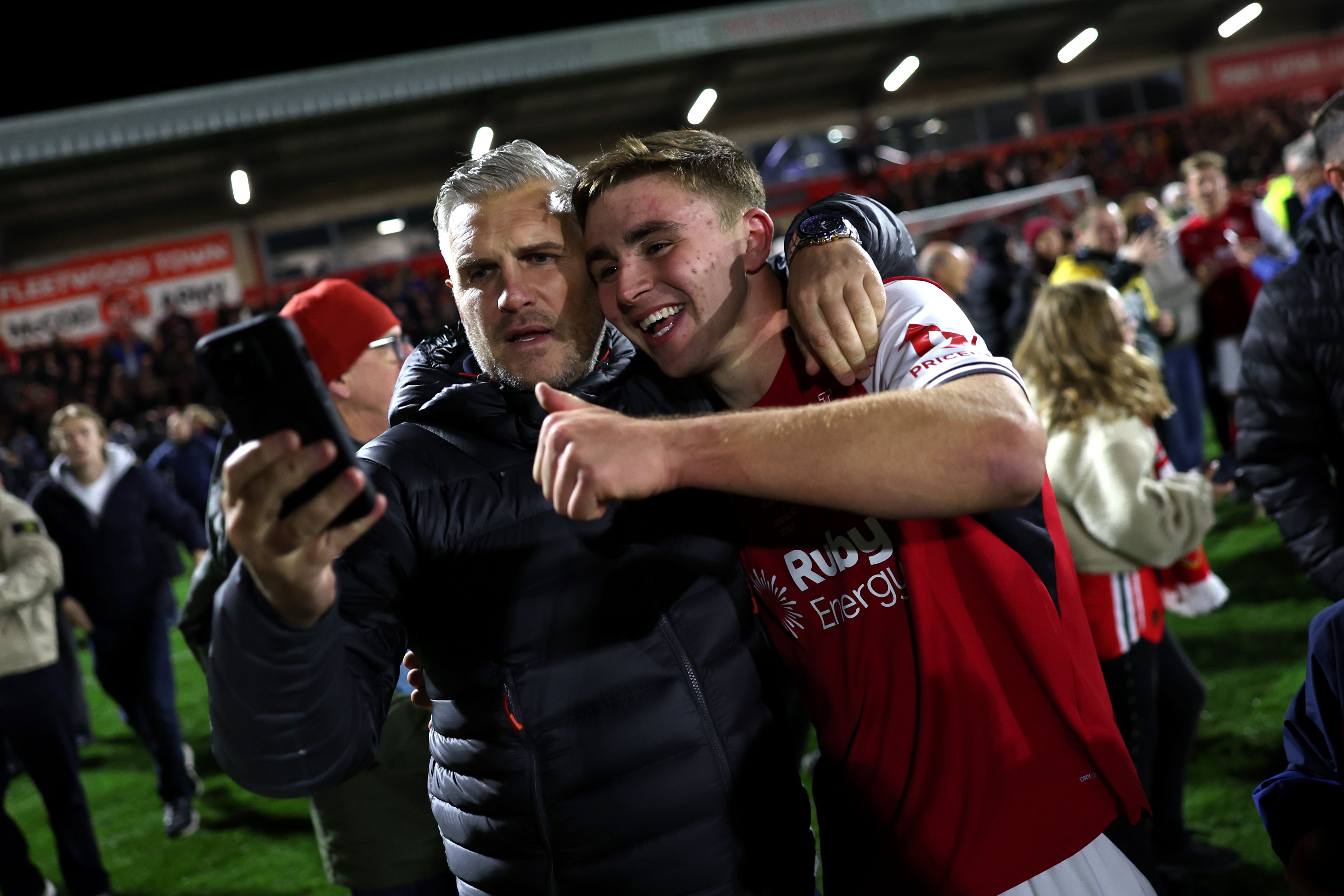 Ein Fußballspieler und ein Fan machen nach dem Spiel auf dem Spielfeld ein Selfie und jubeln.