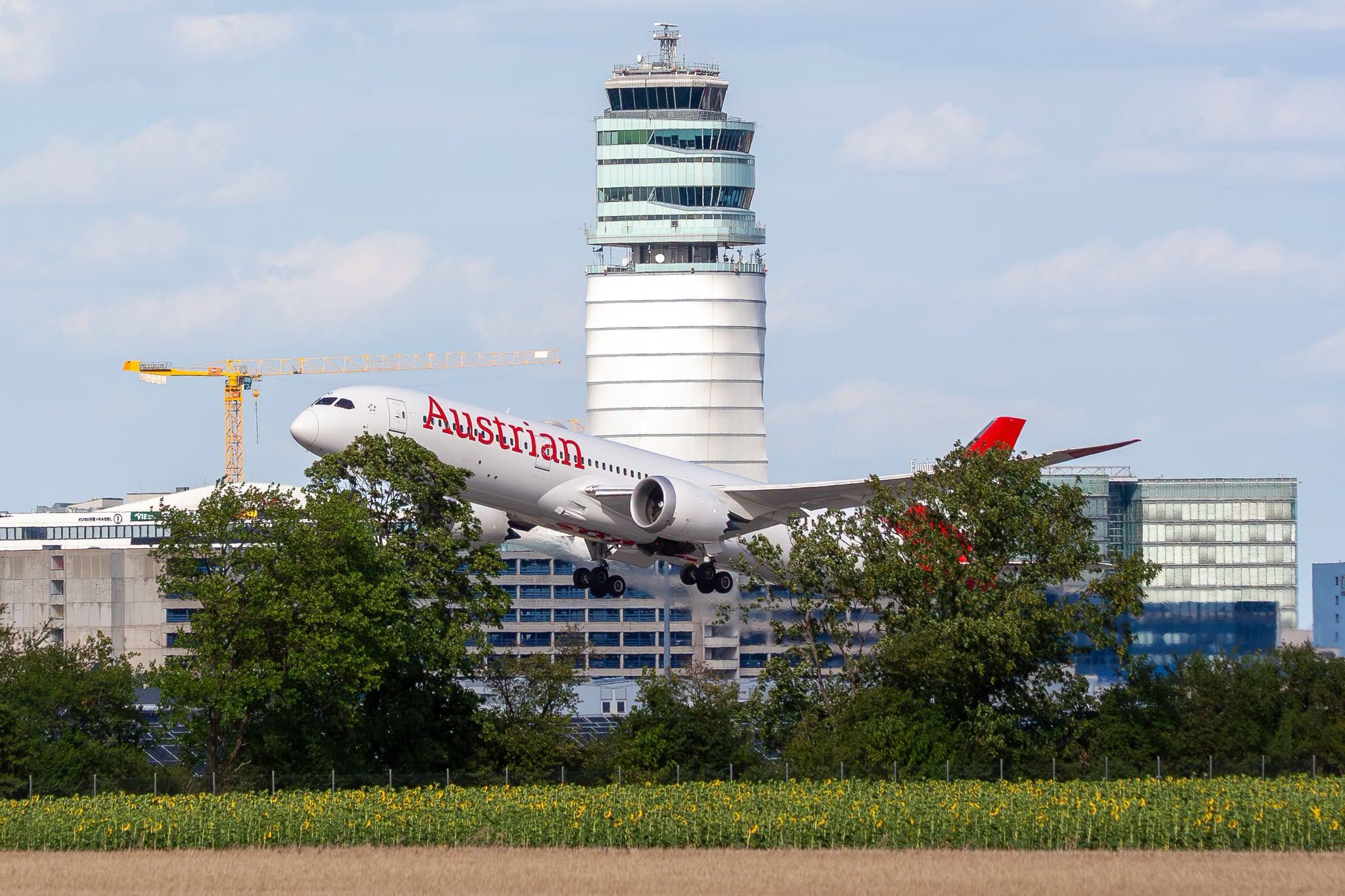 Austrian-Flugzeug startet am Flughafen Wien mit Tower und Gebäuden im Hintergrund.