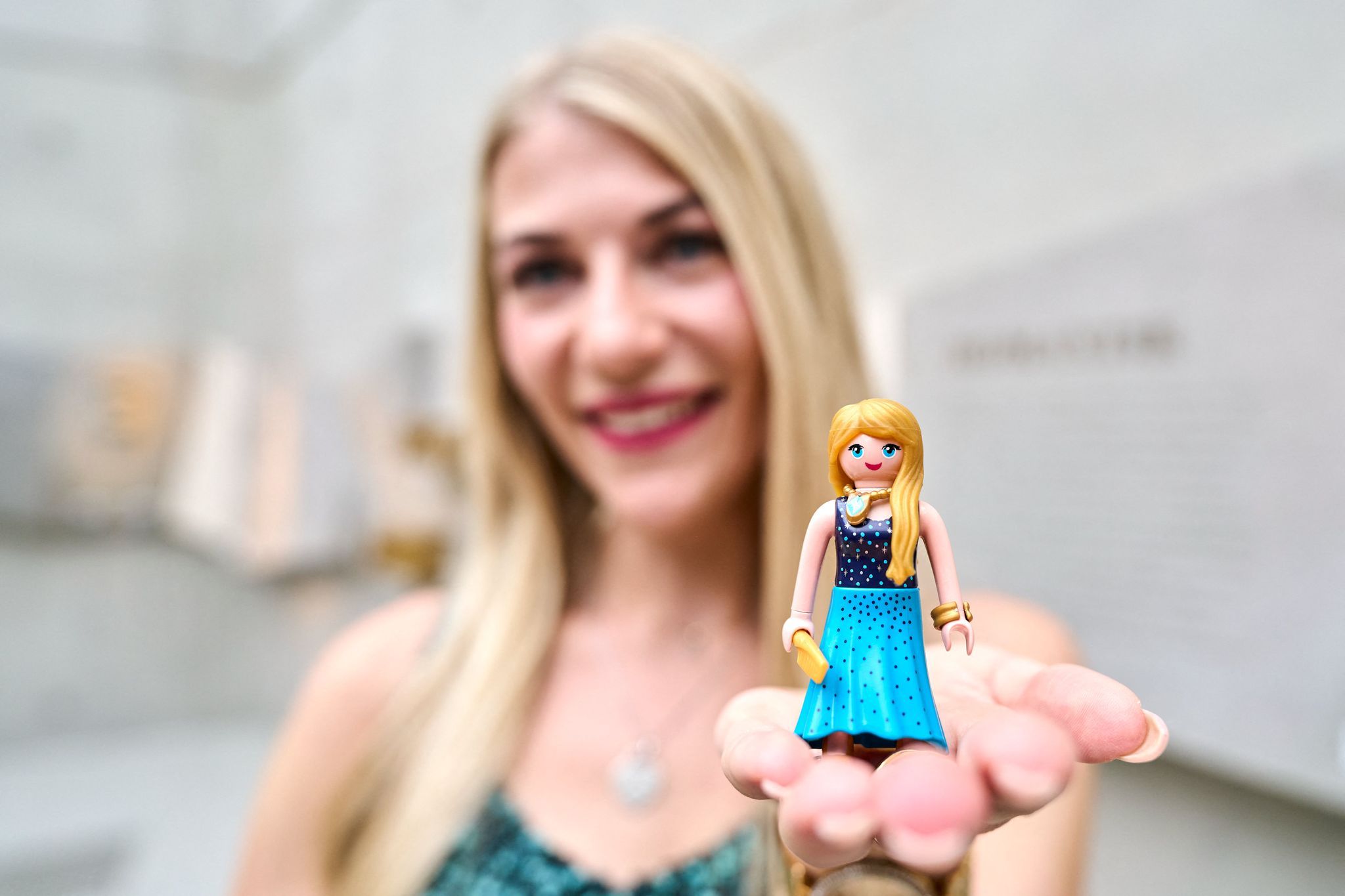 Eine Frau hält eine Playmobil-Figur mit blonden Haaren und blauem Kleid in ihrer Hand.