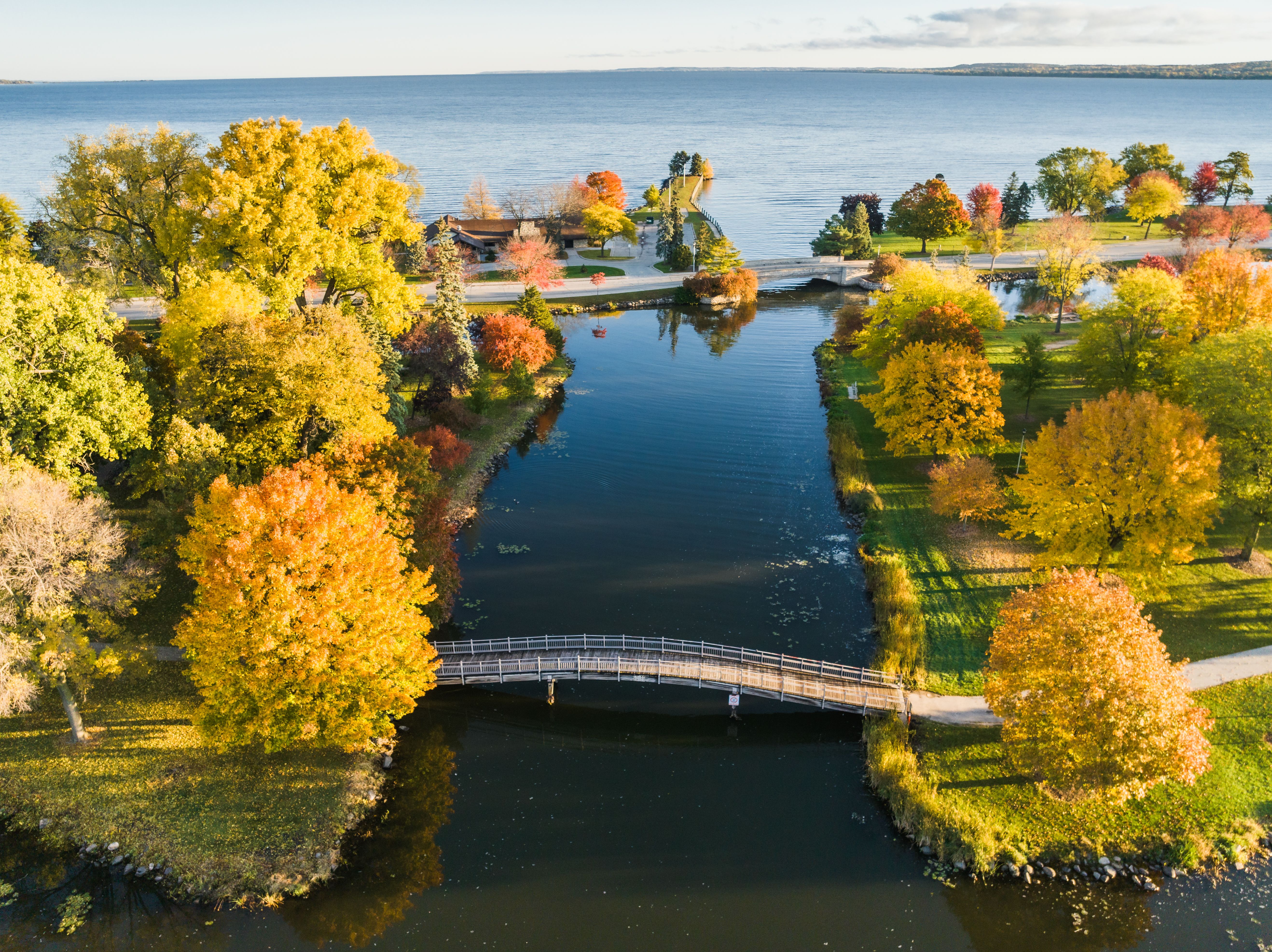 Herbstliche Bäume, ein Fußgängersteg und Wasser am Lake Winnebago in Fond du Lac, Wisconsin.