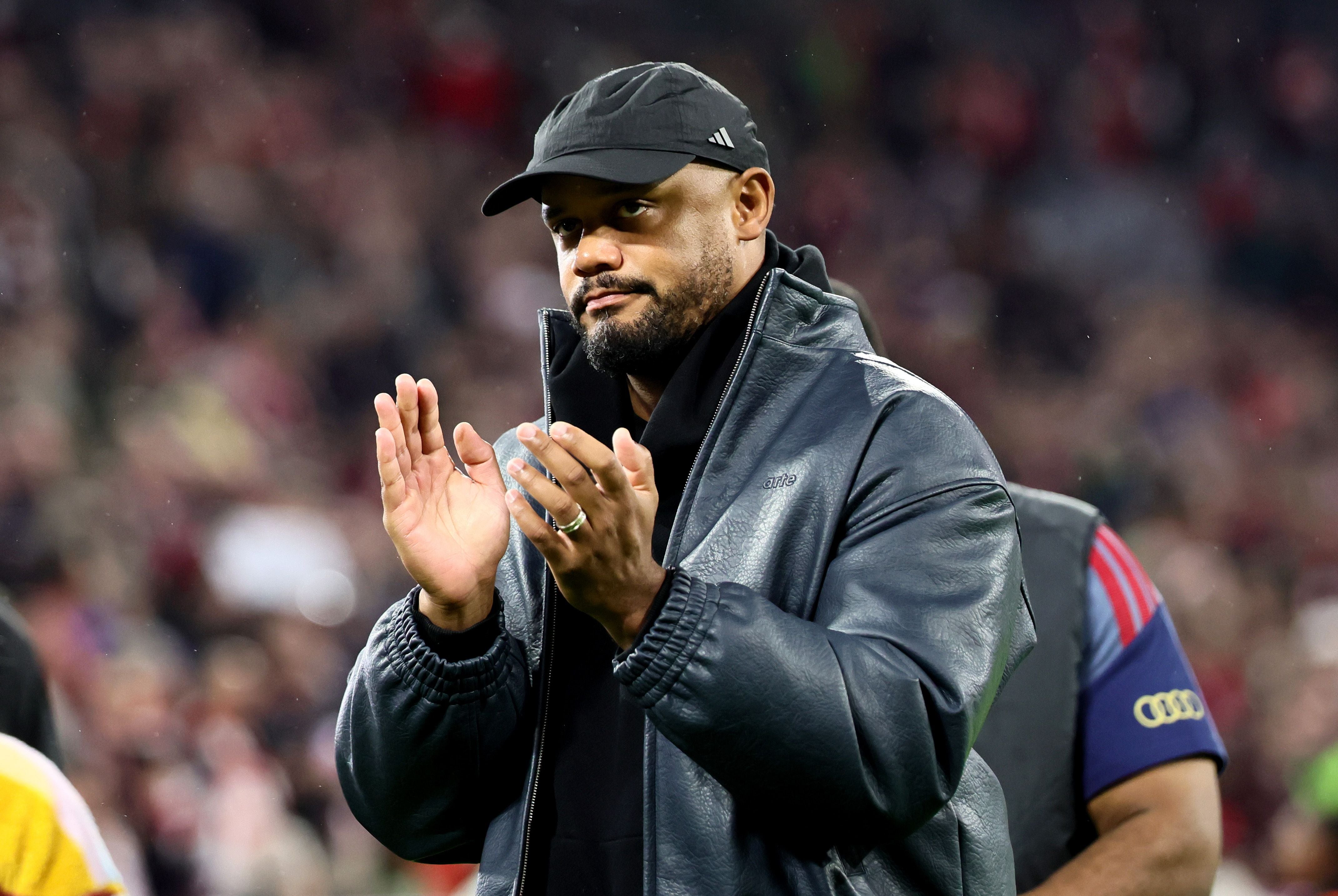 Ein Mann mit schwarzer Kappe und Jacke applaudiert in einem Stadion nach einem Fußballspiel.
