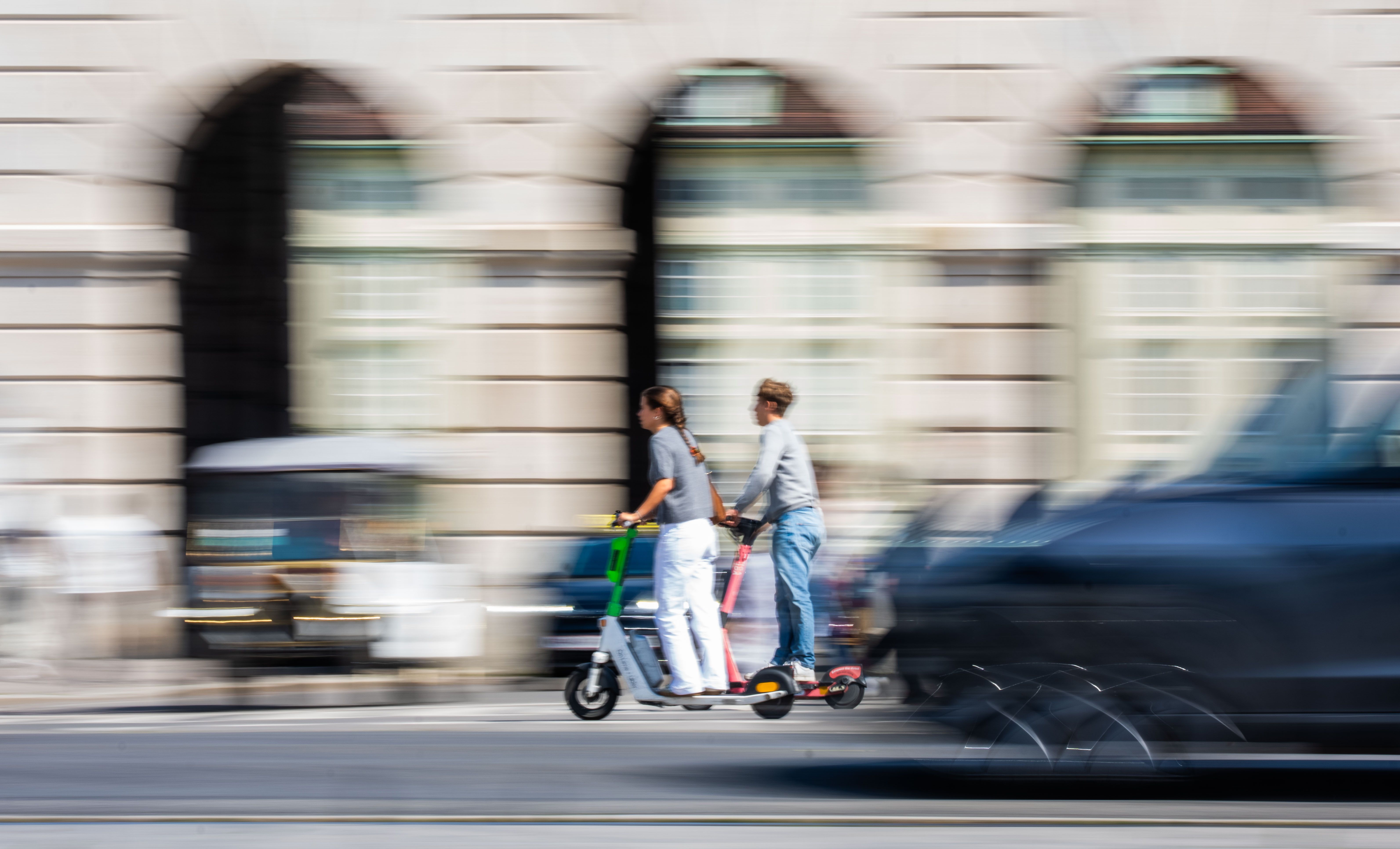 Zwei Personen fahren gemeinsam auf einem E-Scooter durch eine Stadtstraße in Wien.
