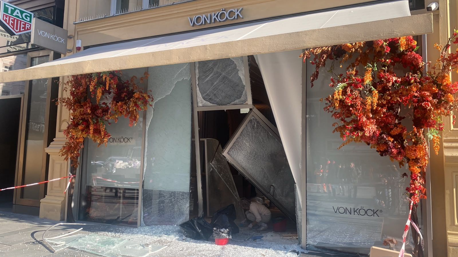Zerstörte Schaufenster eines Juweliers mit herabgefallener Dekoration und Absperrband.