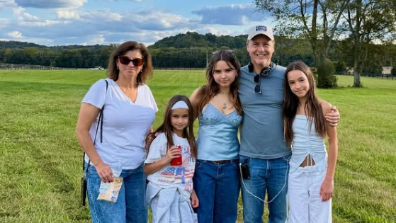 Fünf Personen stehen auf einer Wiese und lächeln in die Kamera, im Hintergrund Bäume und Hügel.
