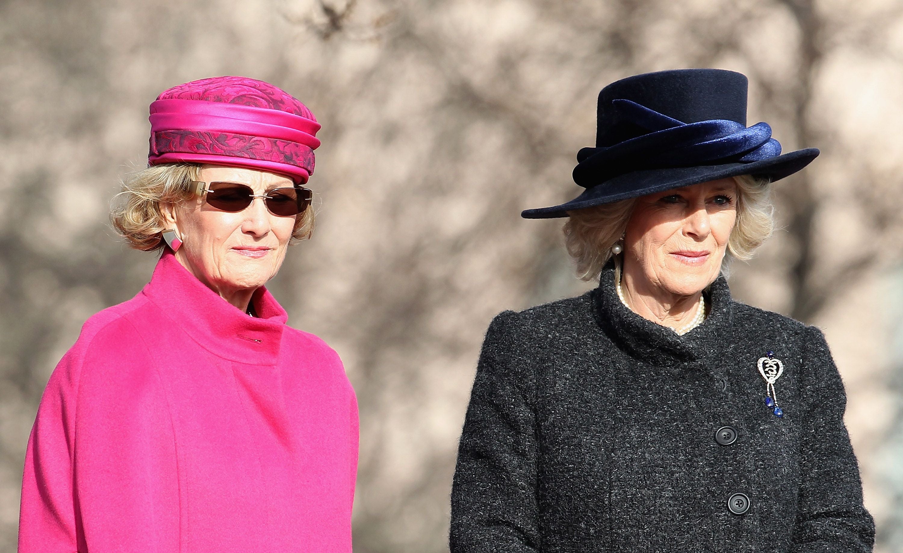 Zwei elegant gekleidete Frauen mit Hüten stehen nebeneinander im Freien.