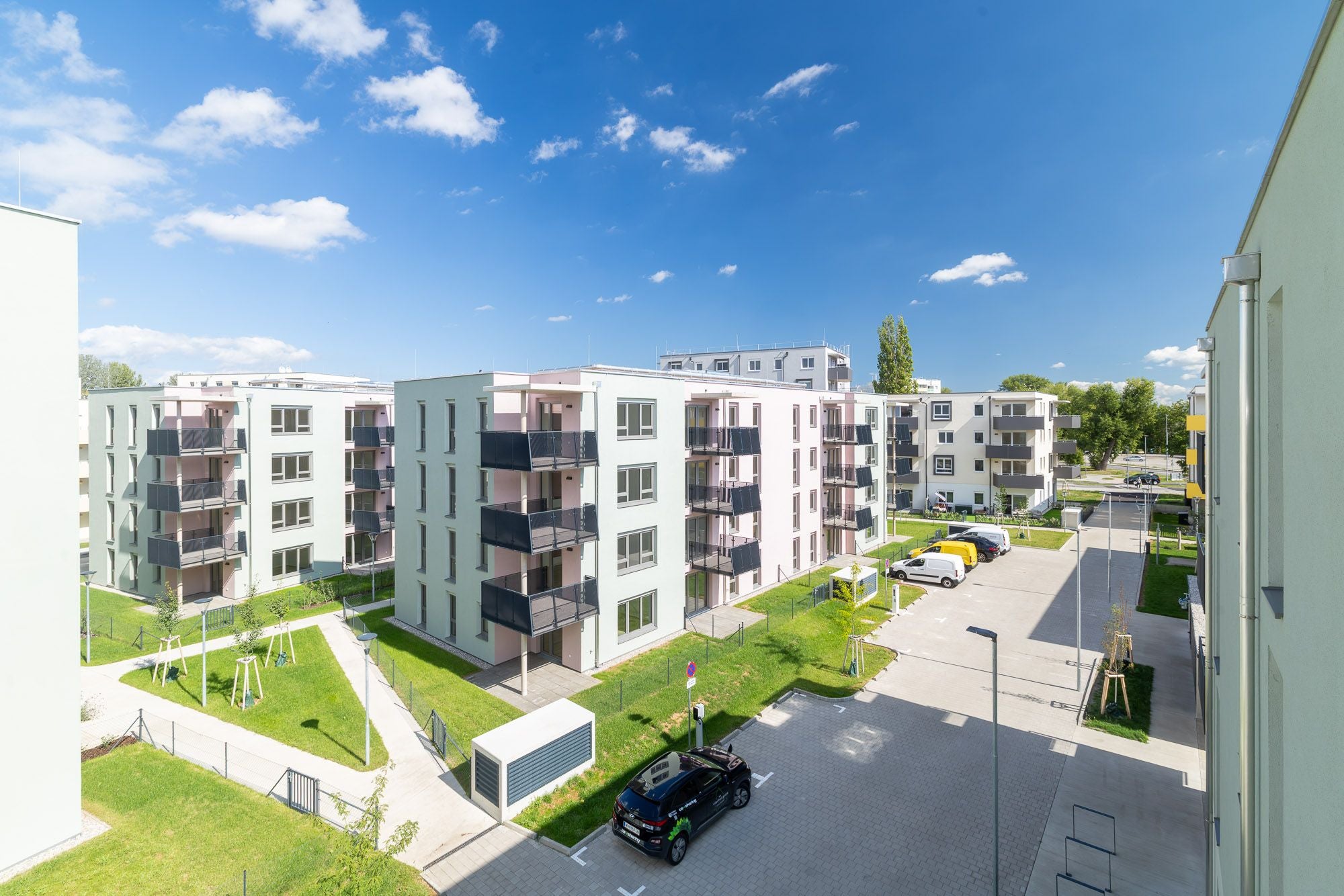 Moderne Wohnhäuser mit Balkonen, gepflegten Grünflächen und geparkten Autos an einem sonnigen Tag.