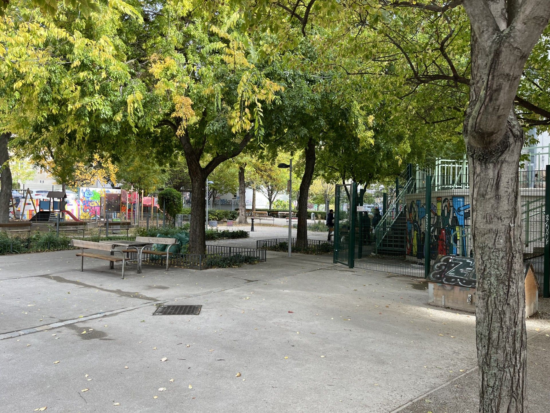 Grüner Park mit Bänken, Bäumen, Spielplatz und bemalter Mauer an der Gumpendorferstraße.