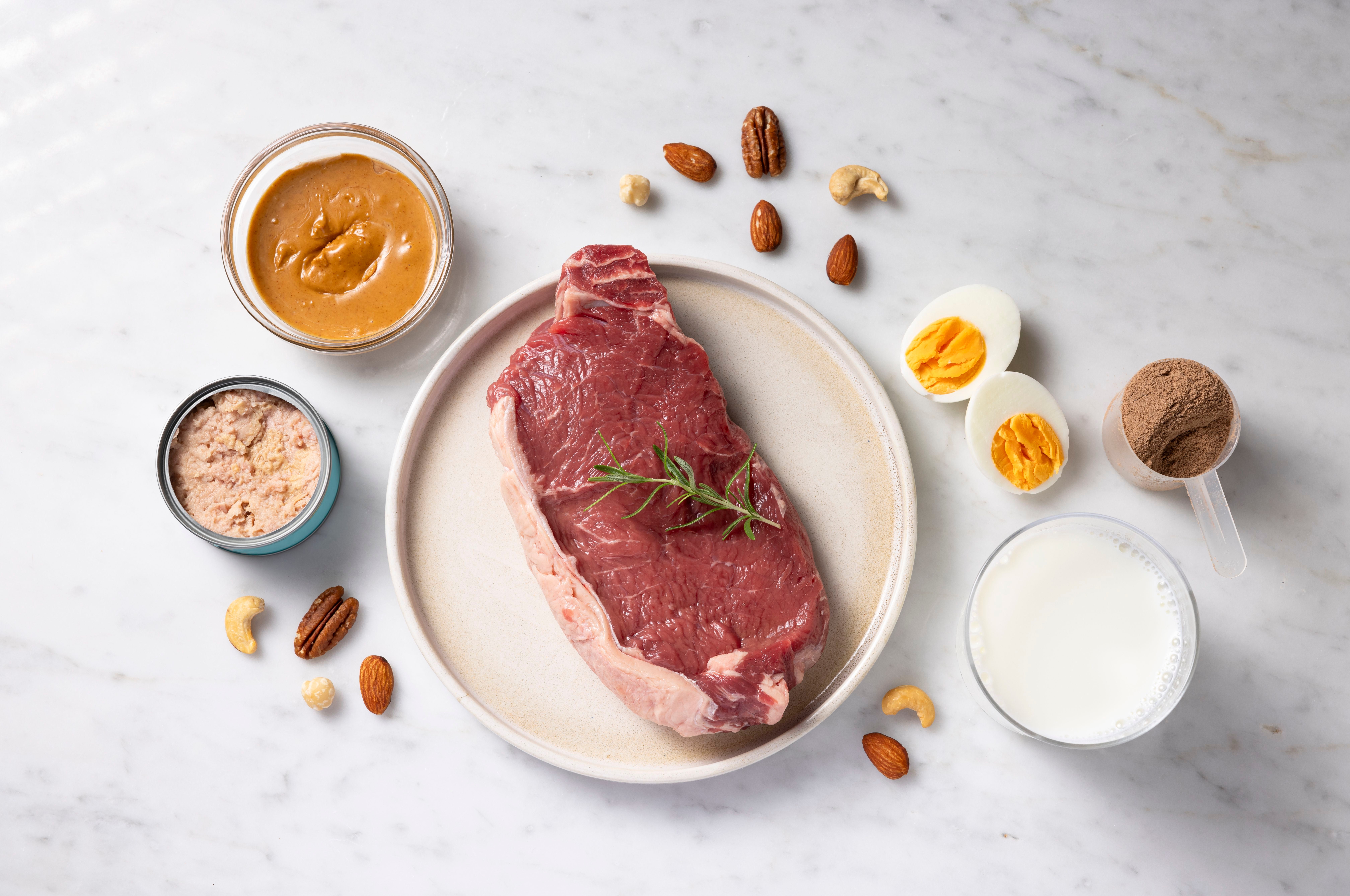 Verschiedene proteinreiche Lebensmittel wie Steak, Eier, Thunfisch, Milch, Nüsse und Erdnussbutter.