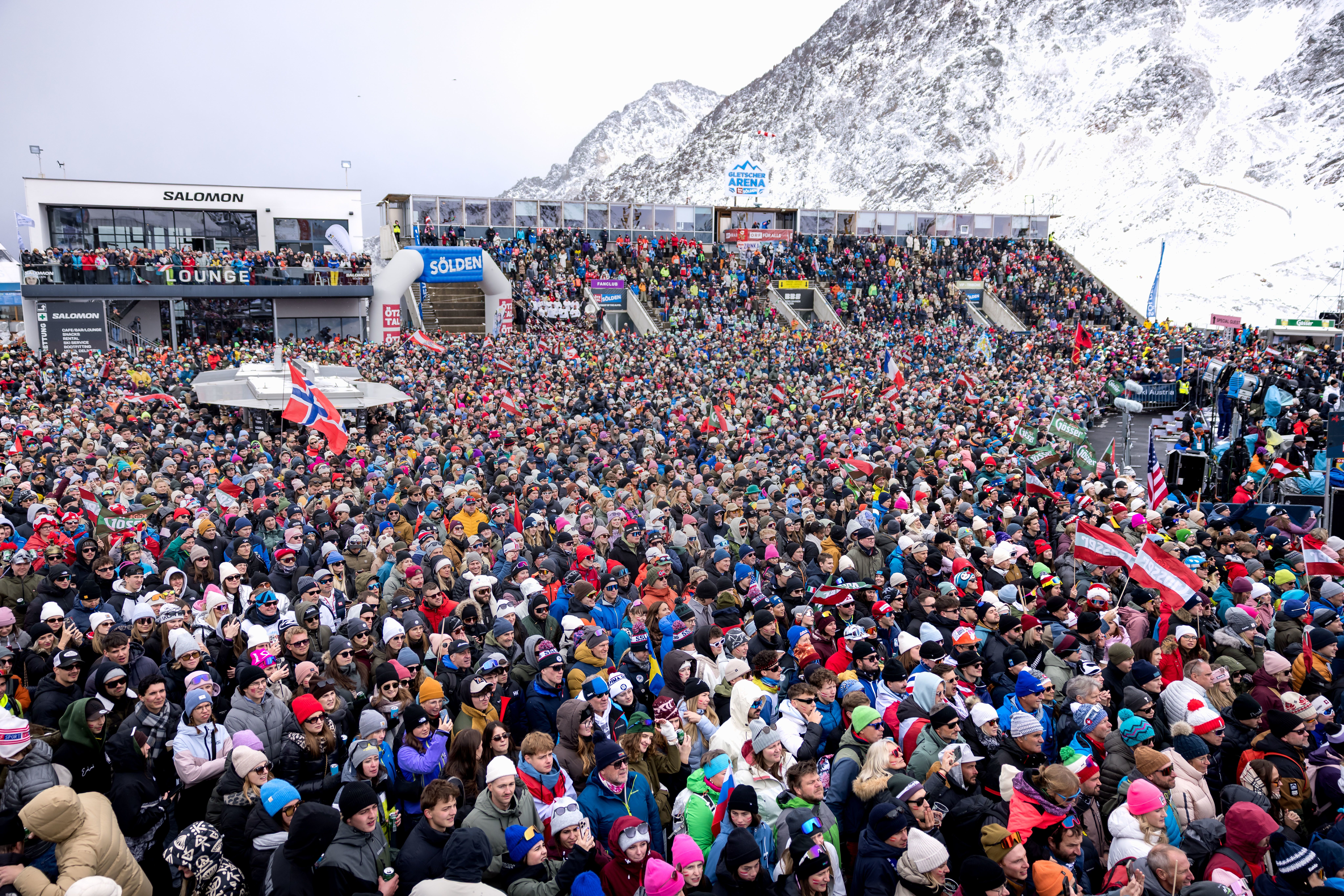 Große Menschenmenge jubelt im Zielbereich eines Ski-Weltcup-Rennens in Sölden vor verschneiten Bergen.