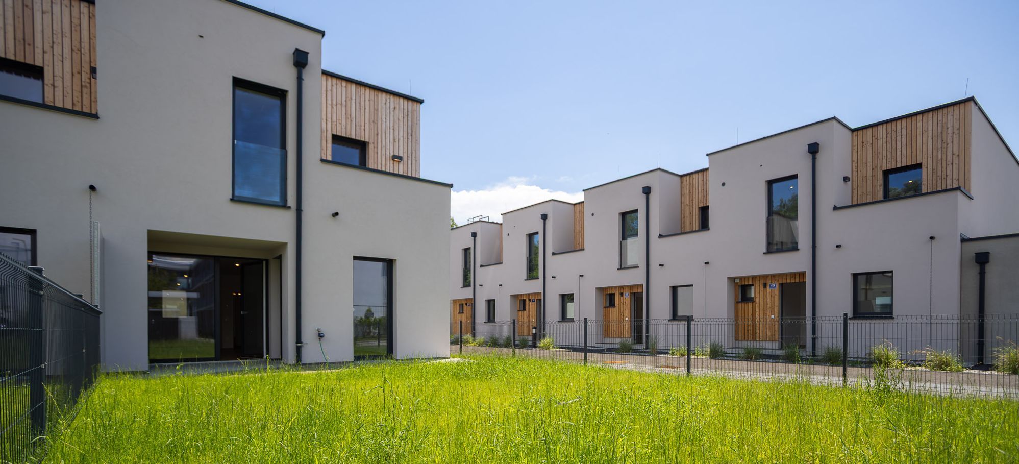 Moderne Reihenhäuser mit großen Fenstern und Holzverkleidung, umgeben von grünem Rasen.
