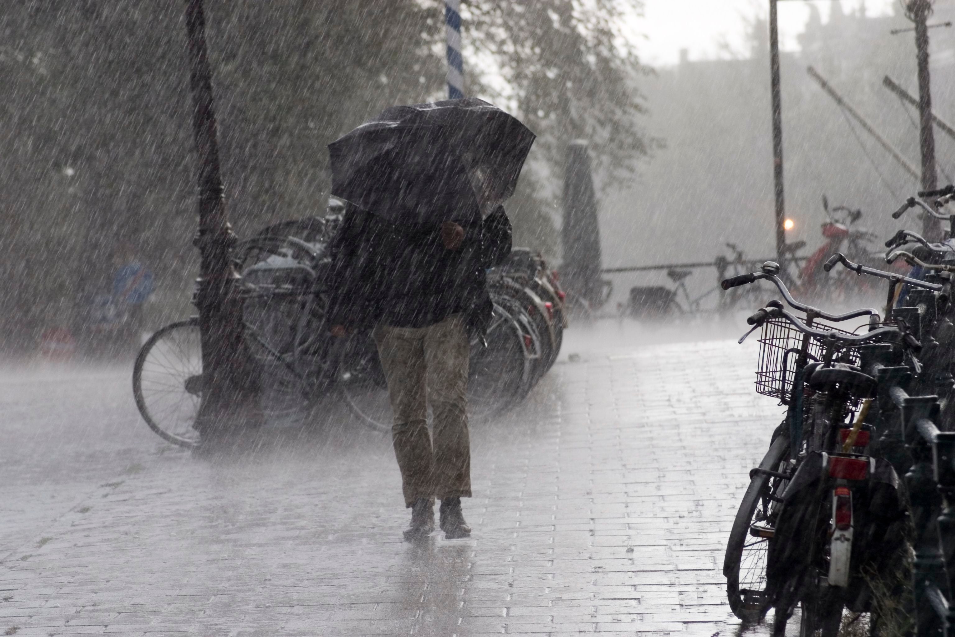 Person mit Regenschirm läuft bei starkem Regen an geparkten Fahrrädern vorbei.